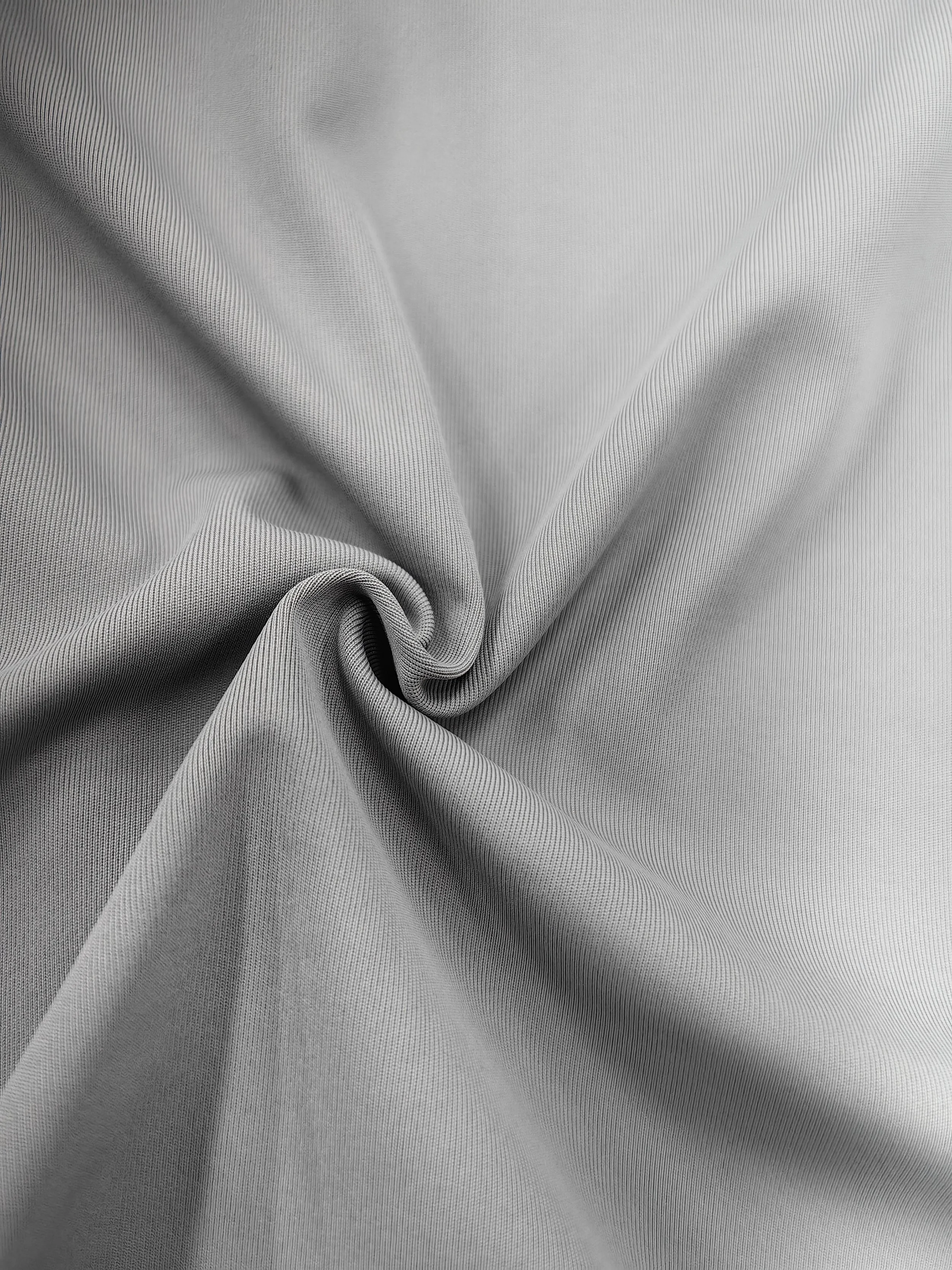 Close-up of a silver or gray fabric with a subtle pattern, gathered and twisted at the bottom left corner.
