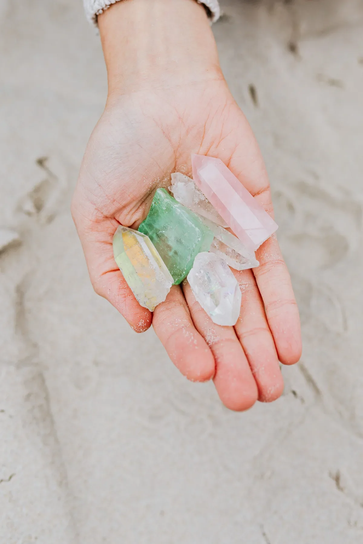Hand holding colorful healing crystals and quartz on sand beach