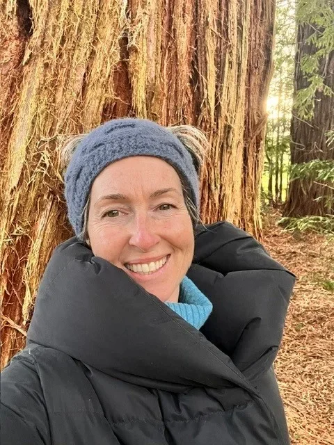 Sara Roberts smiling selfie in front of a giant redwood tree in winter woodland