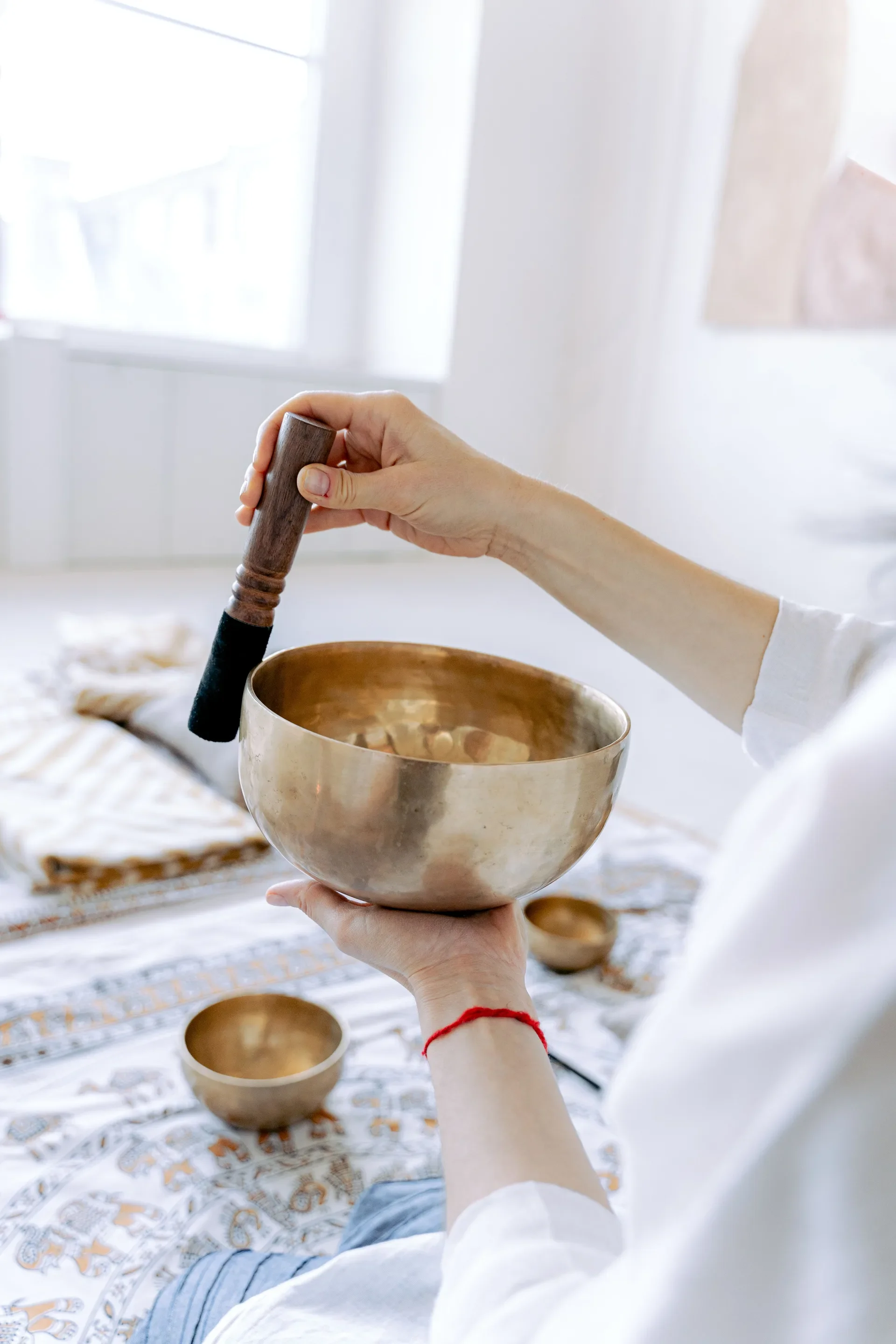 Woman striking brass singing bowl with mallet for sound healing meditation