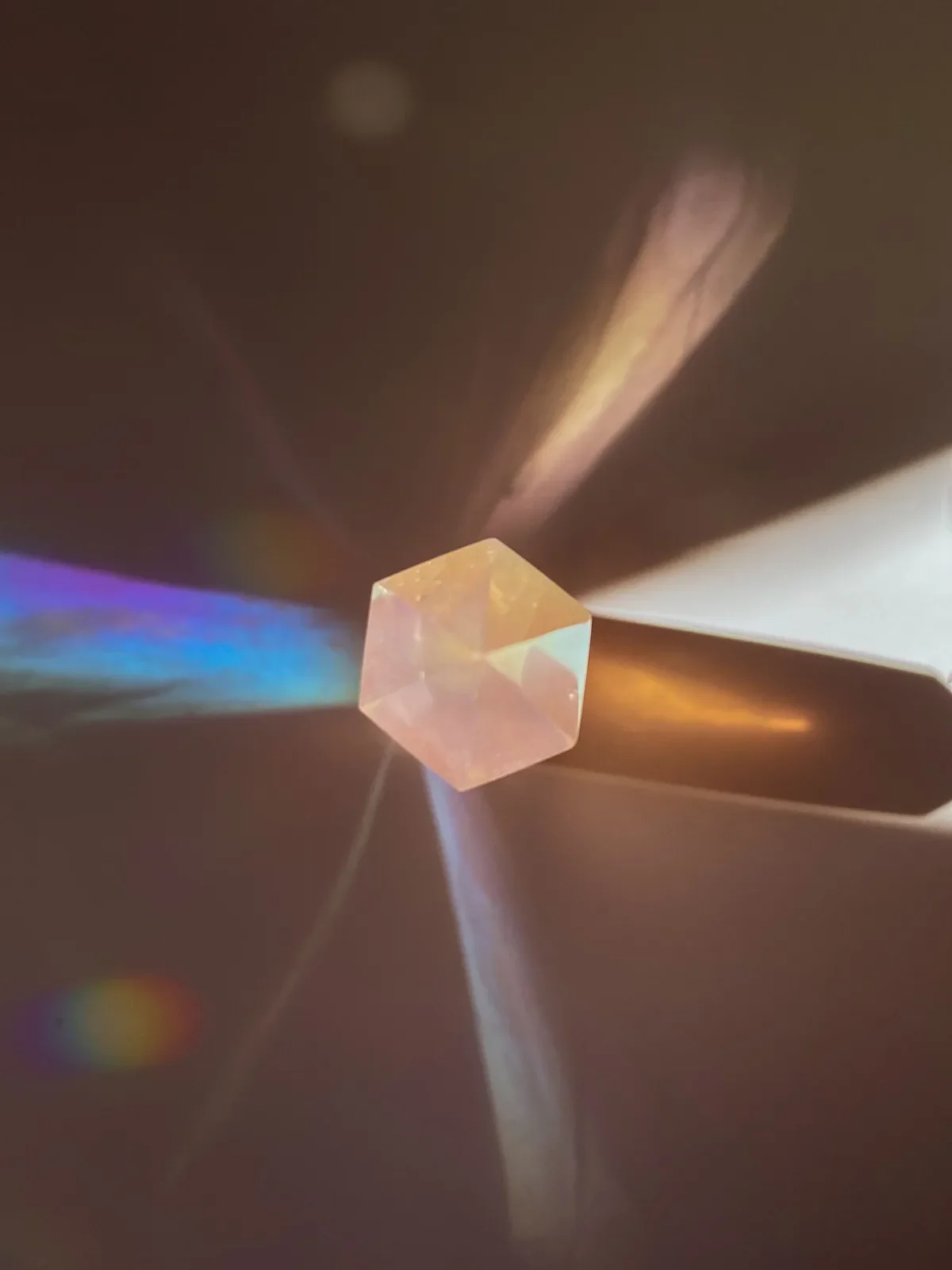 Rose quartz crystal prism refracting colorful light rays on dark background