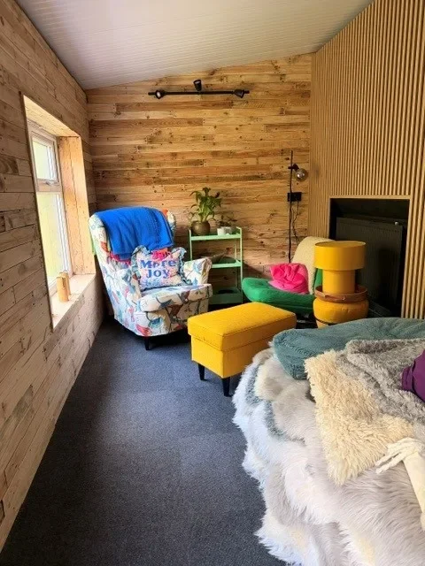 Cozy wood-paneled snug with floral armchair, yellow ottoman, and sheepskin throws for rest and reflection