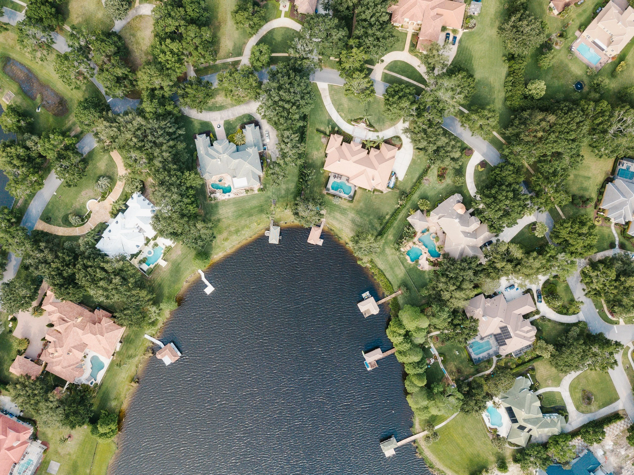 An aerial view of a Florida suburban neighborhood with houses, green lawns, trees, a body of water, and winding sidewalks.