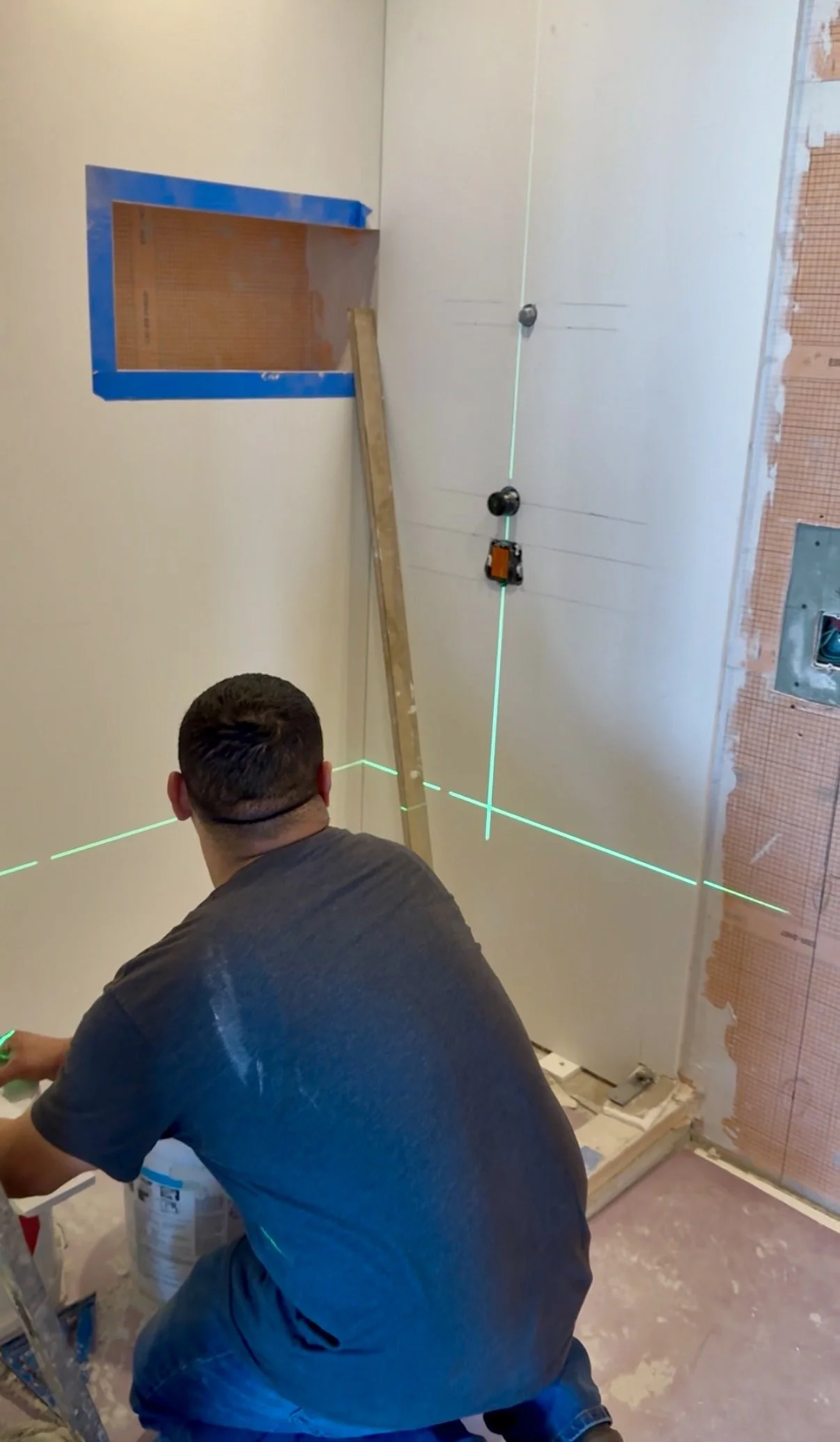 Person working on installing a drywall ceiling with laser alignment lines, with a wooden ladder and an unfinished wall.