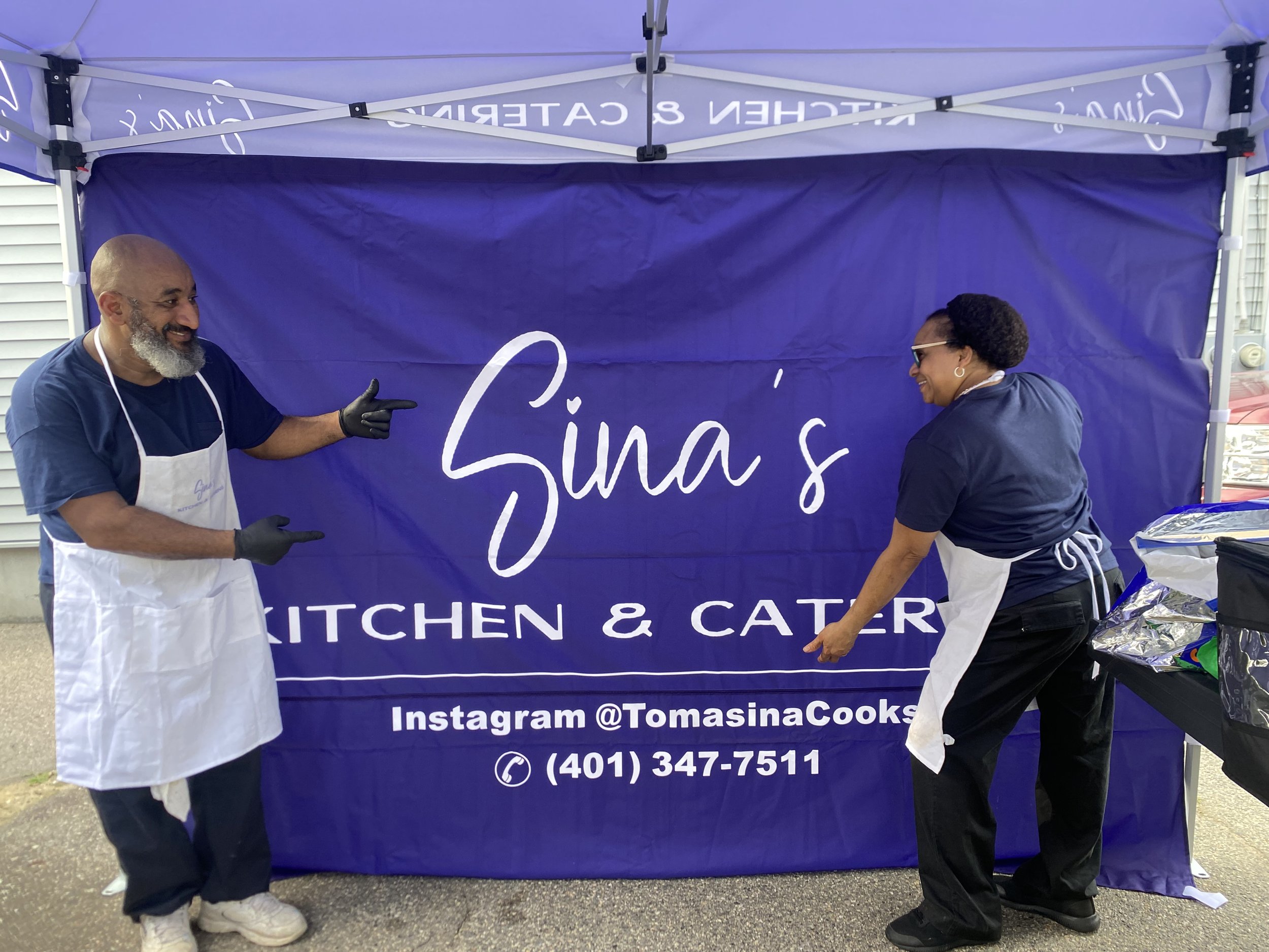 Two smiling people in apron and chef coat at a food booth next to a blue canopy tent with white lettering that reads "Sinas" and contact information.
