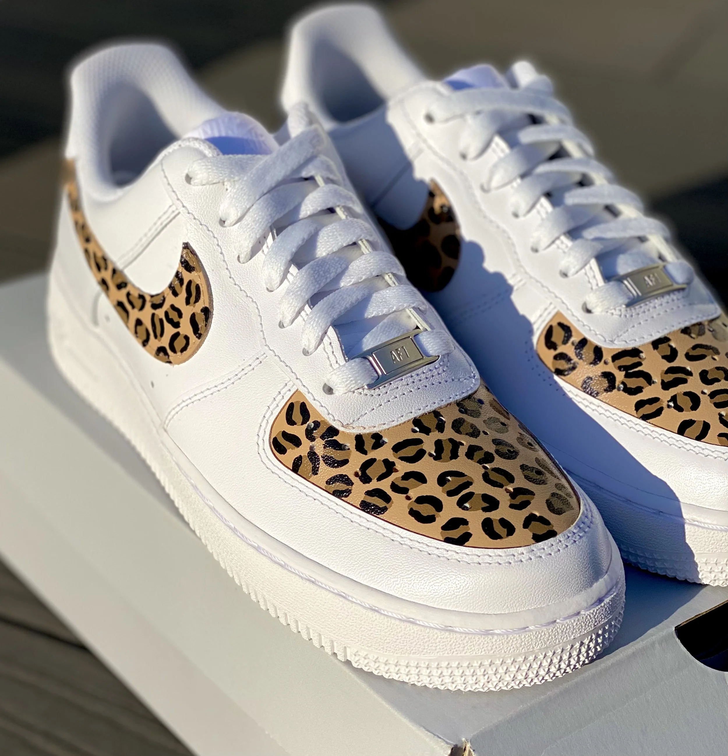 White sneakers with leopard-print accents and metal eyelets on a white surface.