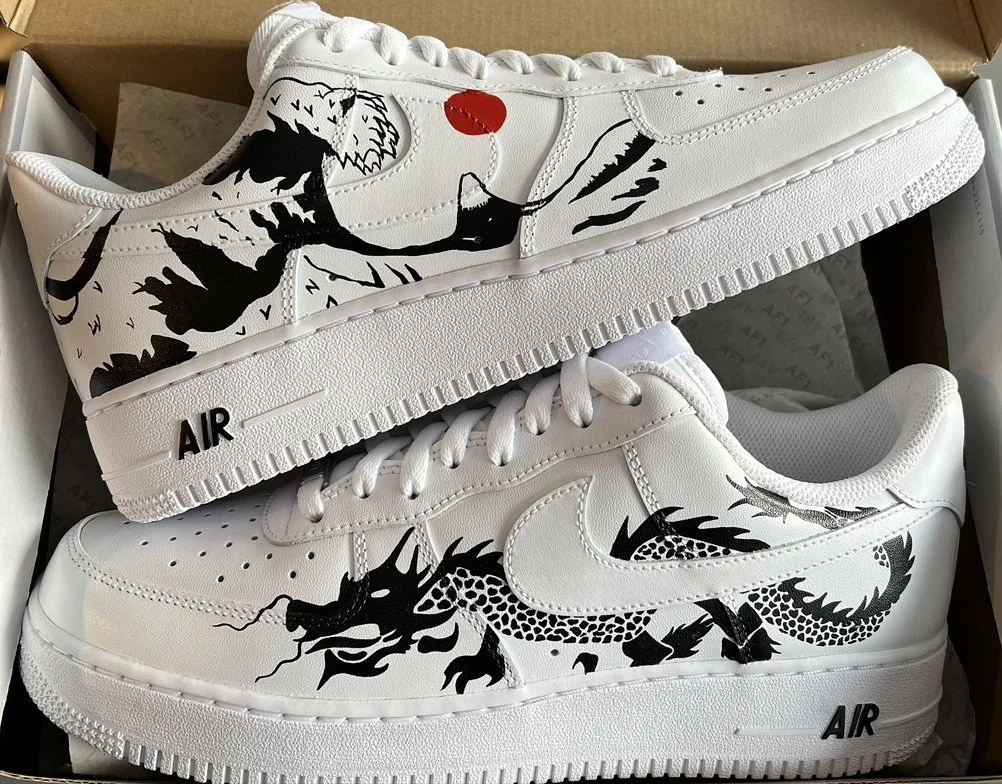 Pair of custom white Nike sneakers with black dragon artwork and a red heart on the upper shoe. The sneakers have 'AIR' written on the midsoles.