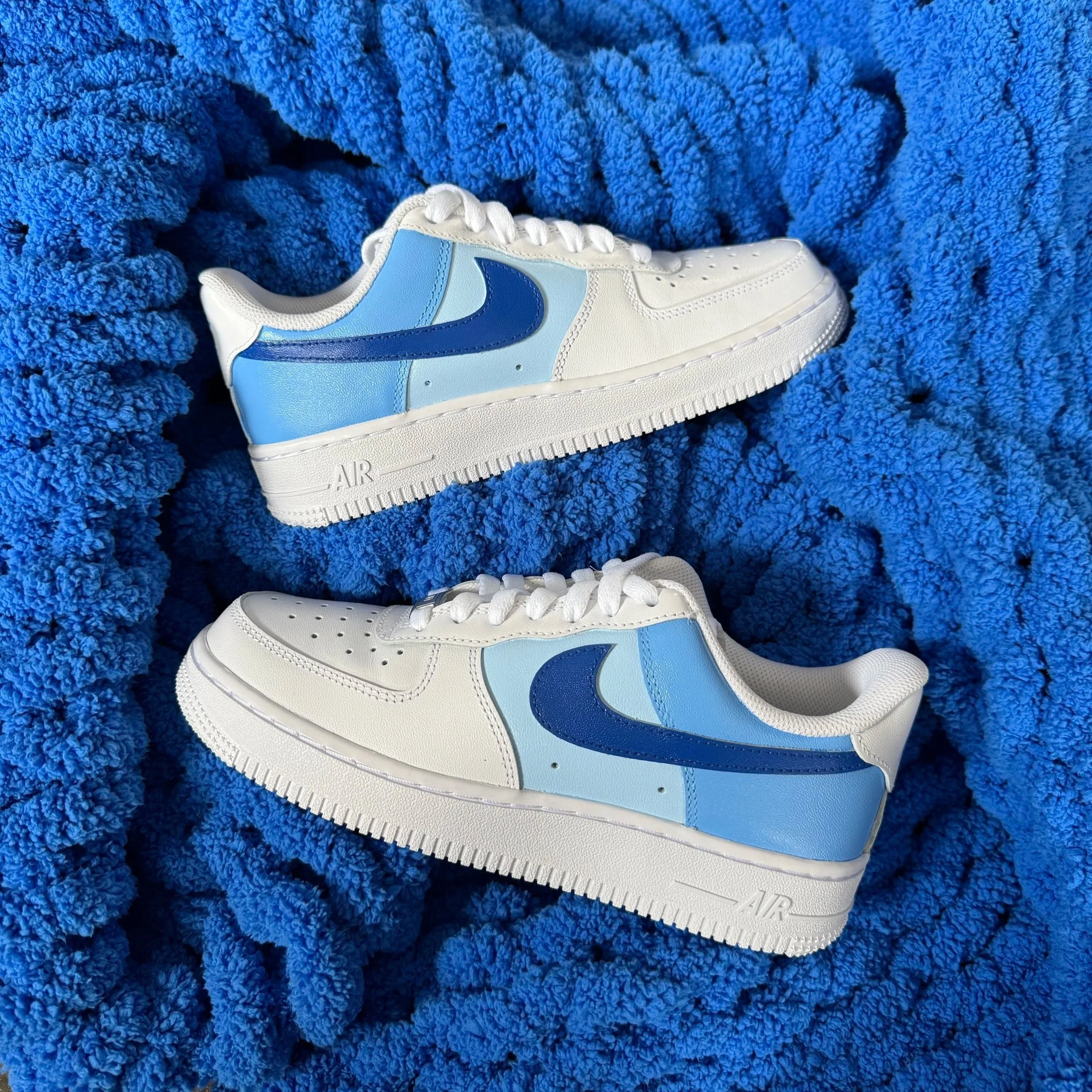 Close-up of white sneakers with blue Nike swoosh, placed on a plush blue textured fabric background.