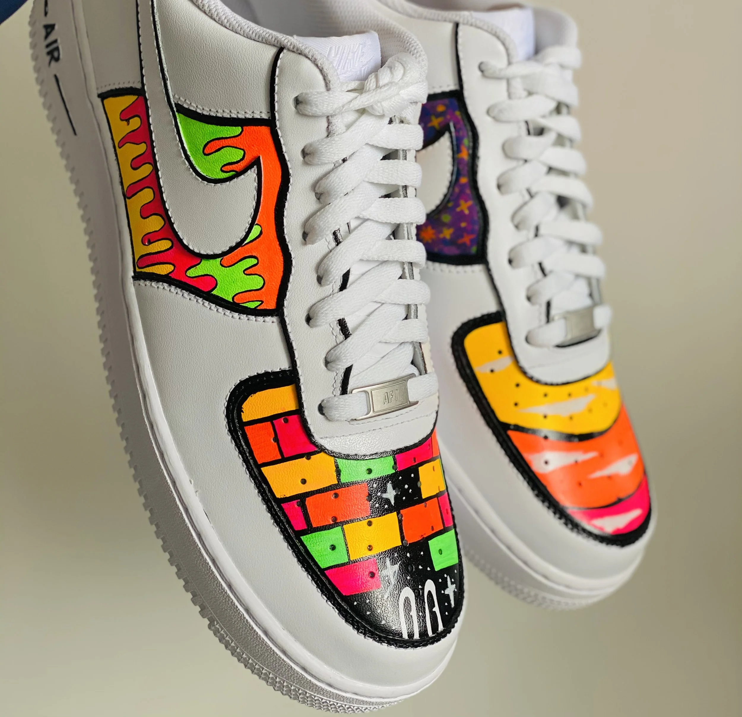 Close-up image of a white sneaker with cartoon-like colorful patches, including a rainbow, stars, and abstract shapes, sewn onto the side.