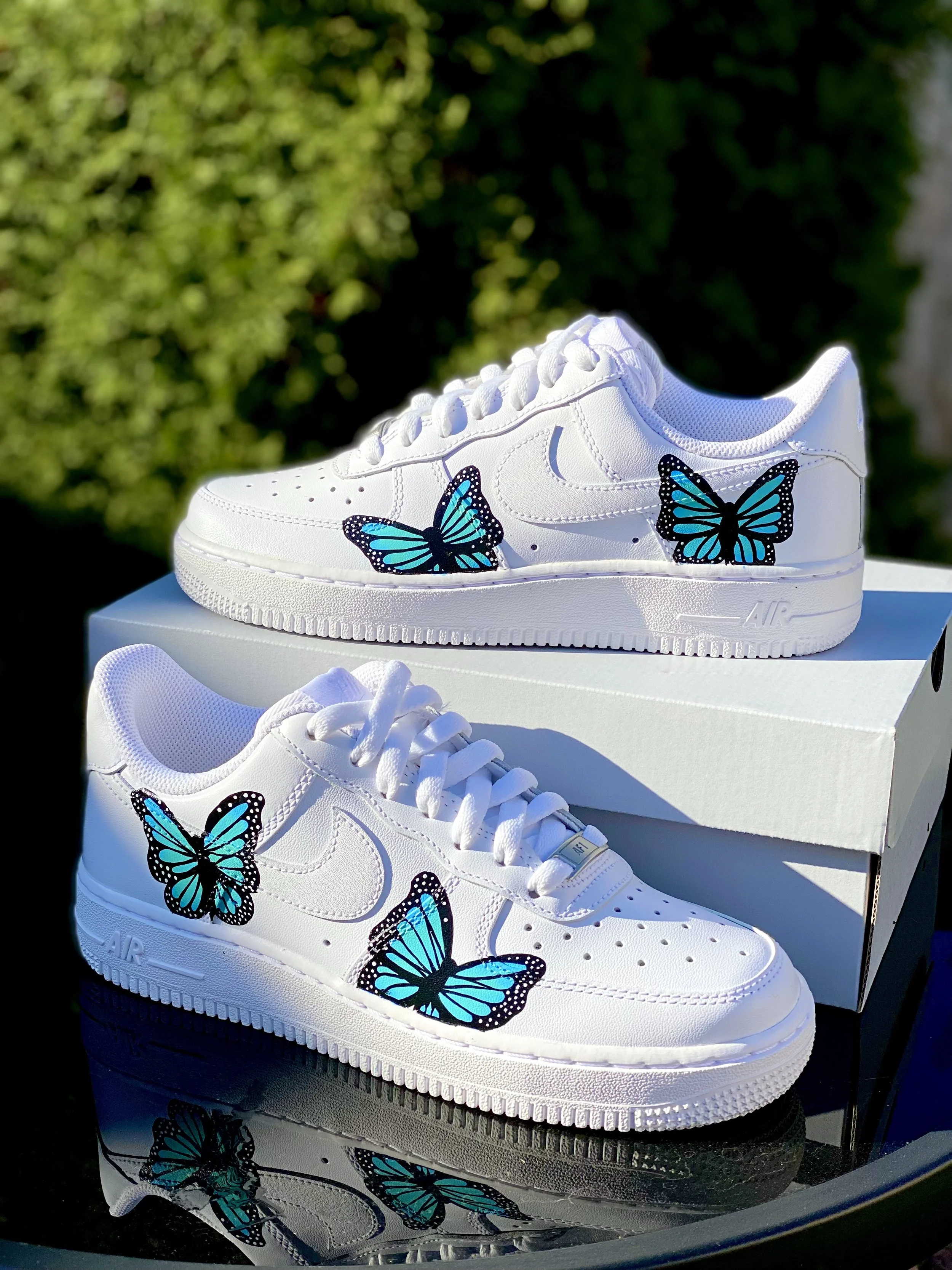 White sneakers with blue butterfly designs displayed on top of their box outdoors during daytime.