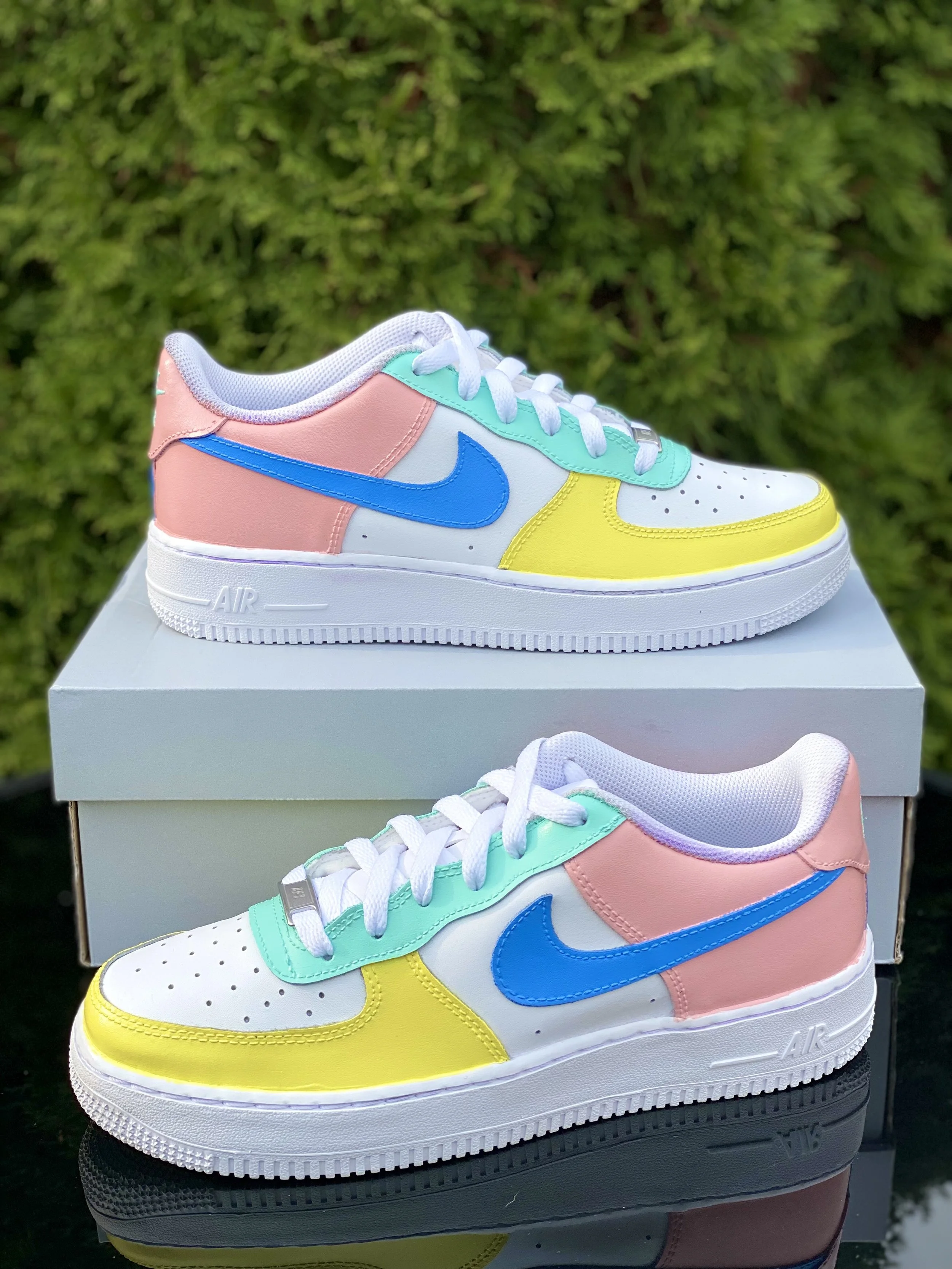 Colorful Nike sneakers with pink, teal, yellow, and blue accents on a white sole, placed on top of a white shoe box.