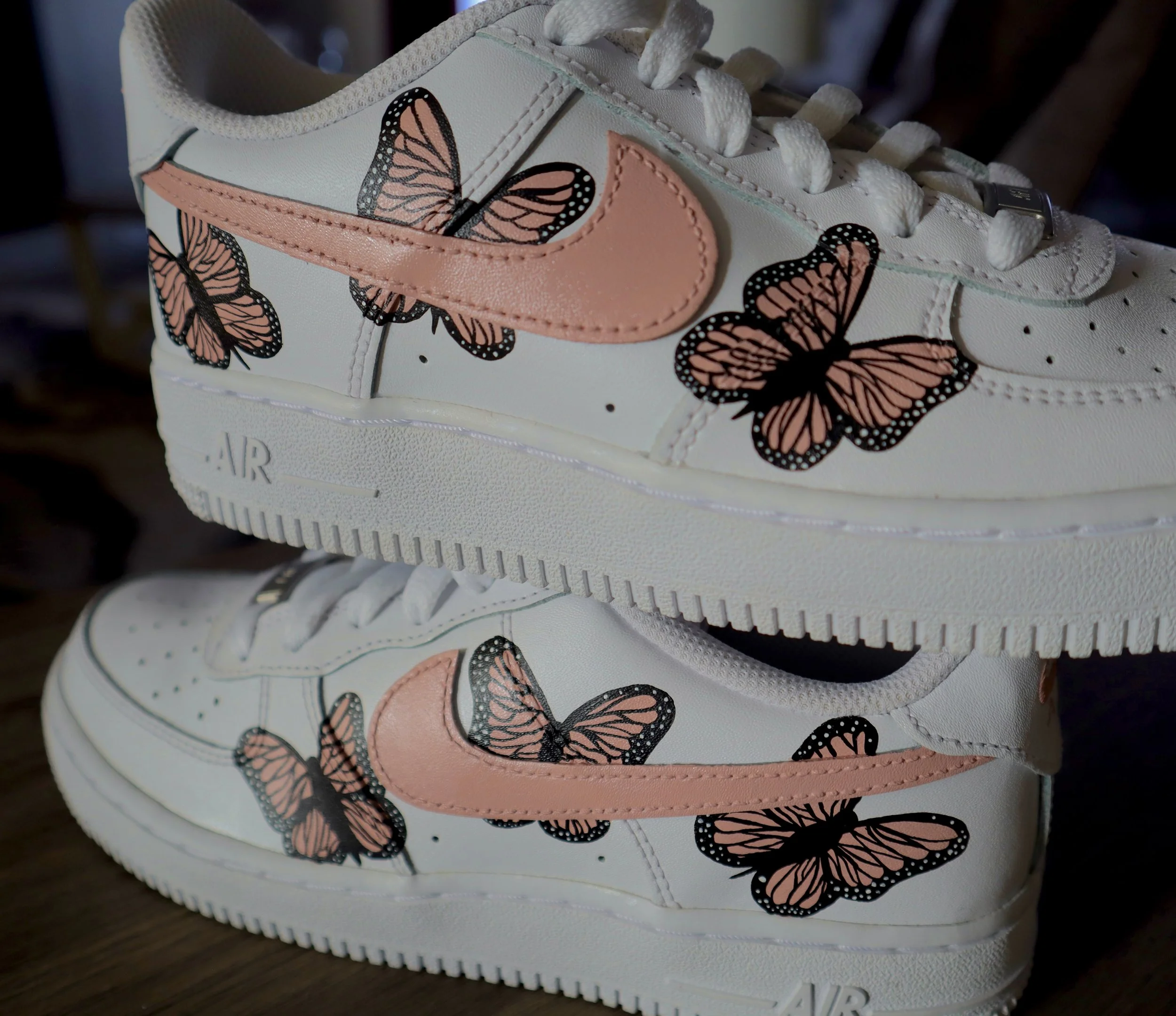 Close-up of a white sneaker with pink accents and black and pink butterfly illustrations on the side.