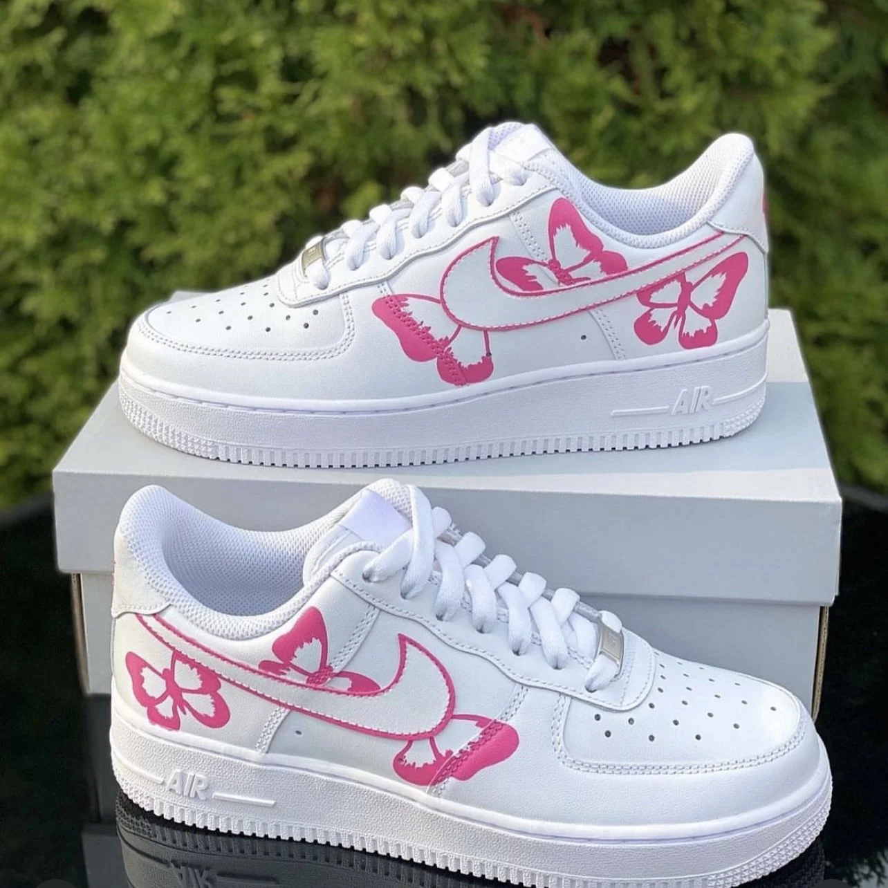 White sneakers with pink butterfly and flower designs, placed on a white shoe box outdoors.