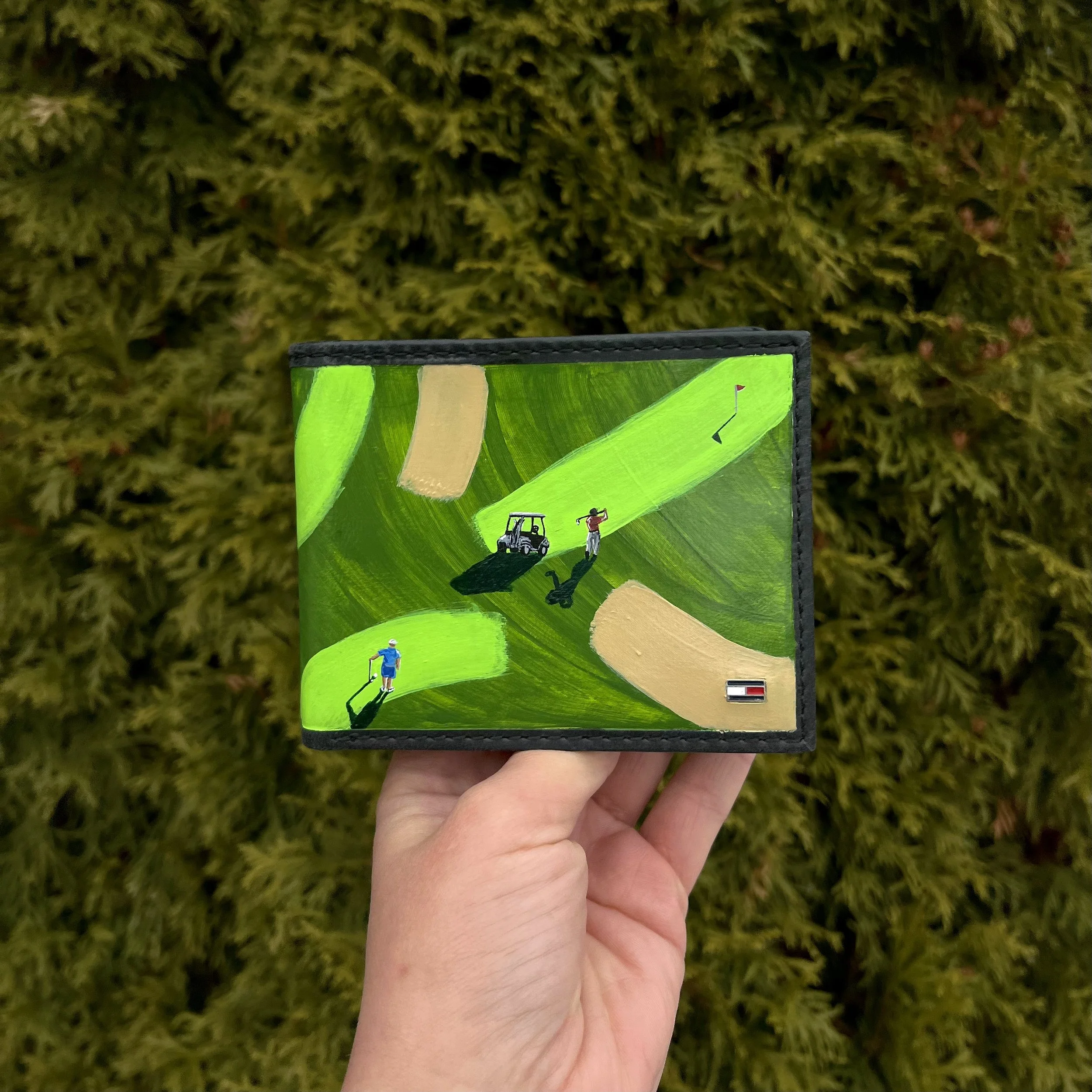 Close-up of a hand holding a colorful illustrated card with golf-related images, with green shrubbery in the background.