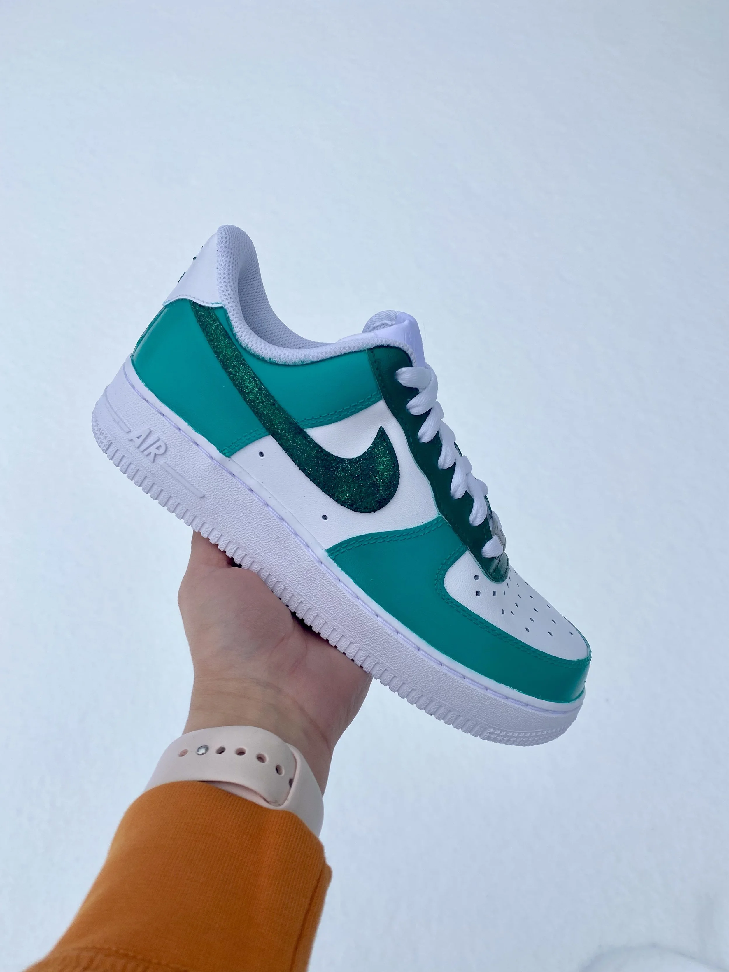A sneaker with white, green, and black colors being held in a person's hand over a snowy surface.