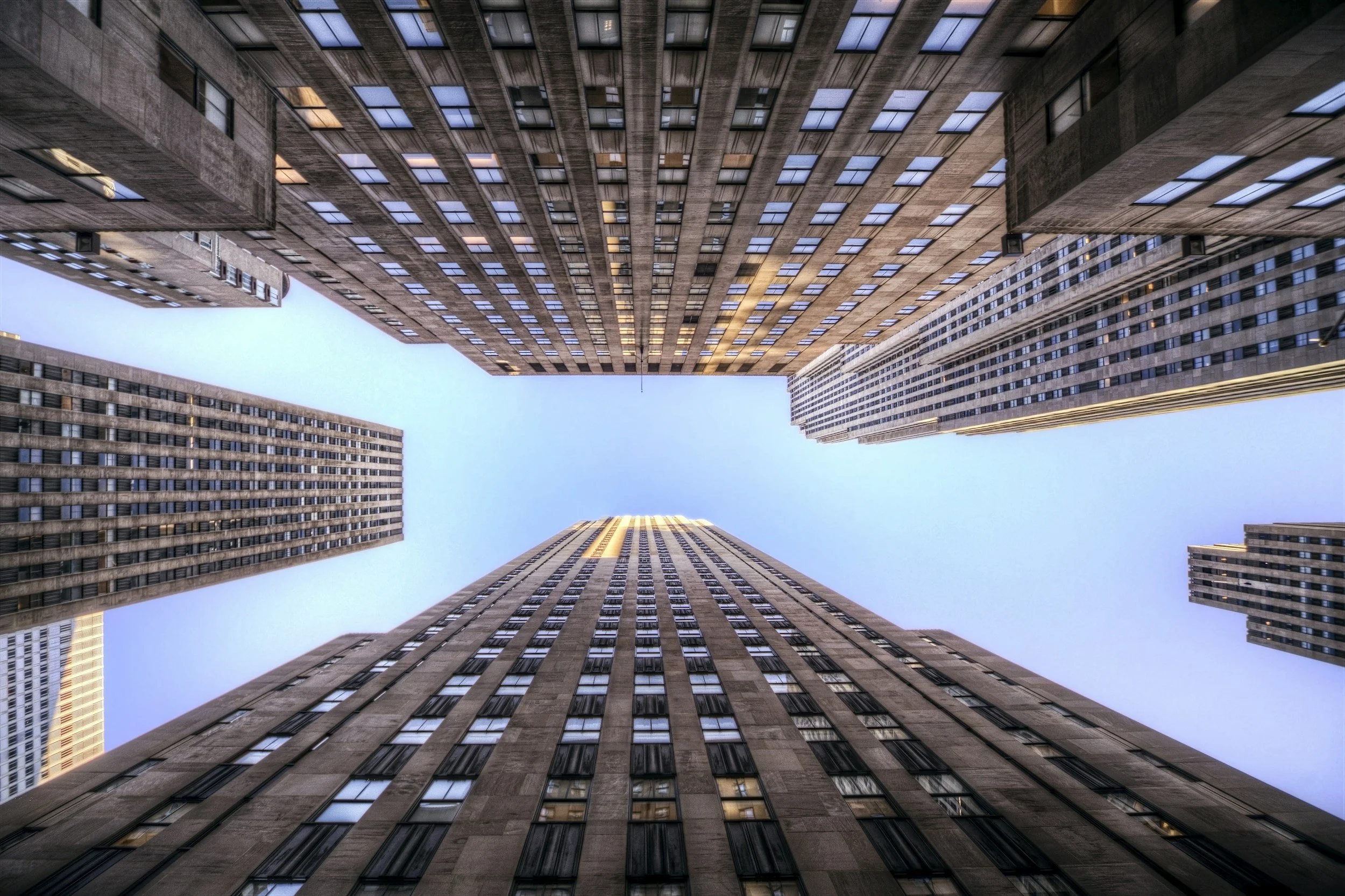 Vues de plusieurs gratte-ciel modernes en hauteur, prises depuis le sol vers le ciel, montrant les façades en béton et en verre avec plusieurs fenêtres.