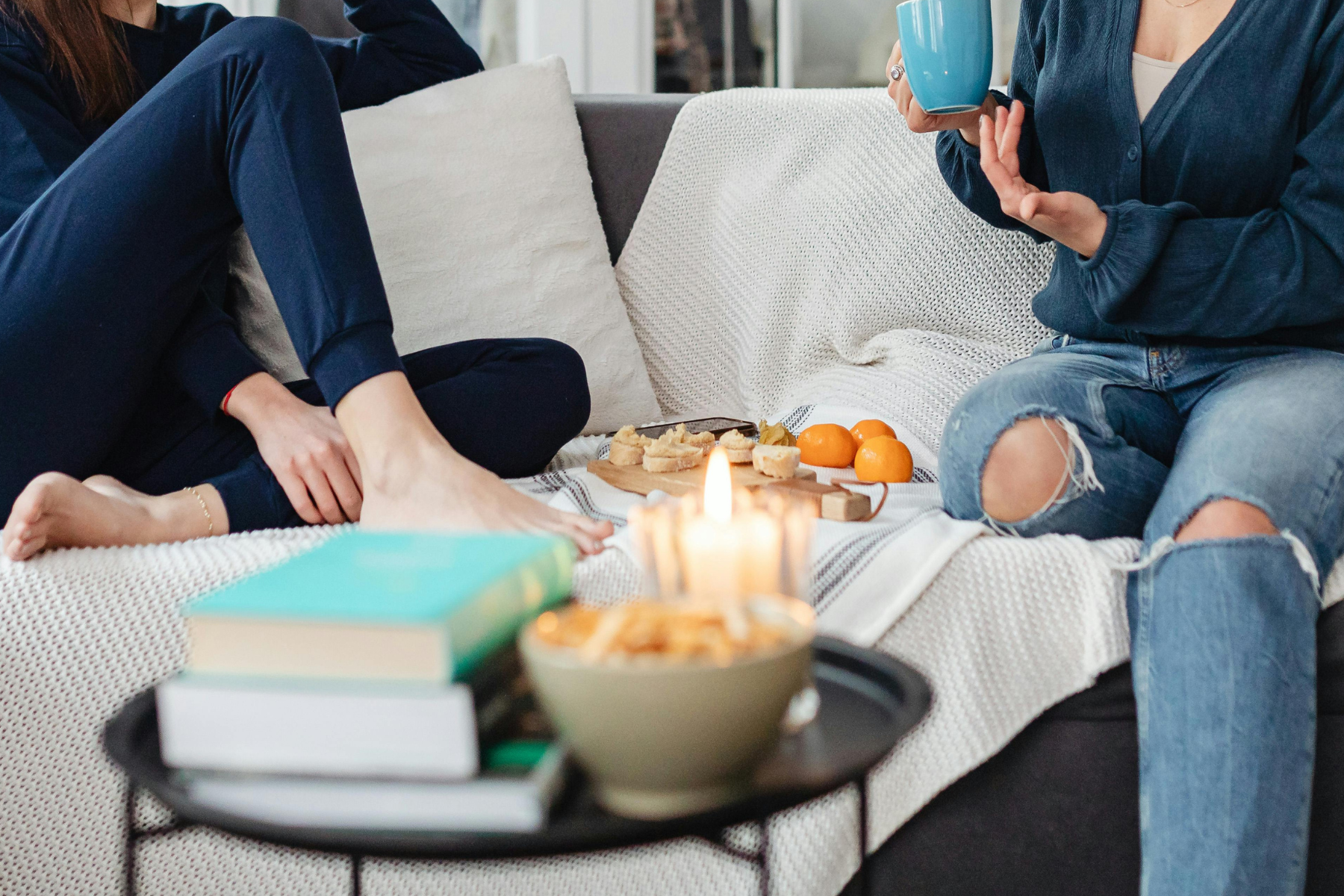 Women relaxing together on a couch with tea, snacks, and candlelight.