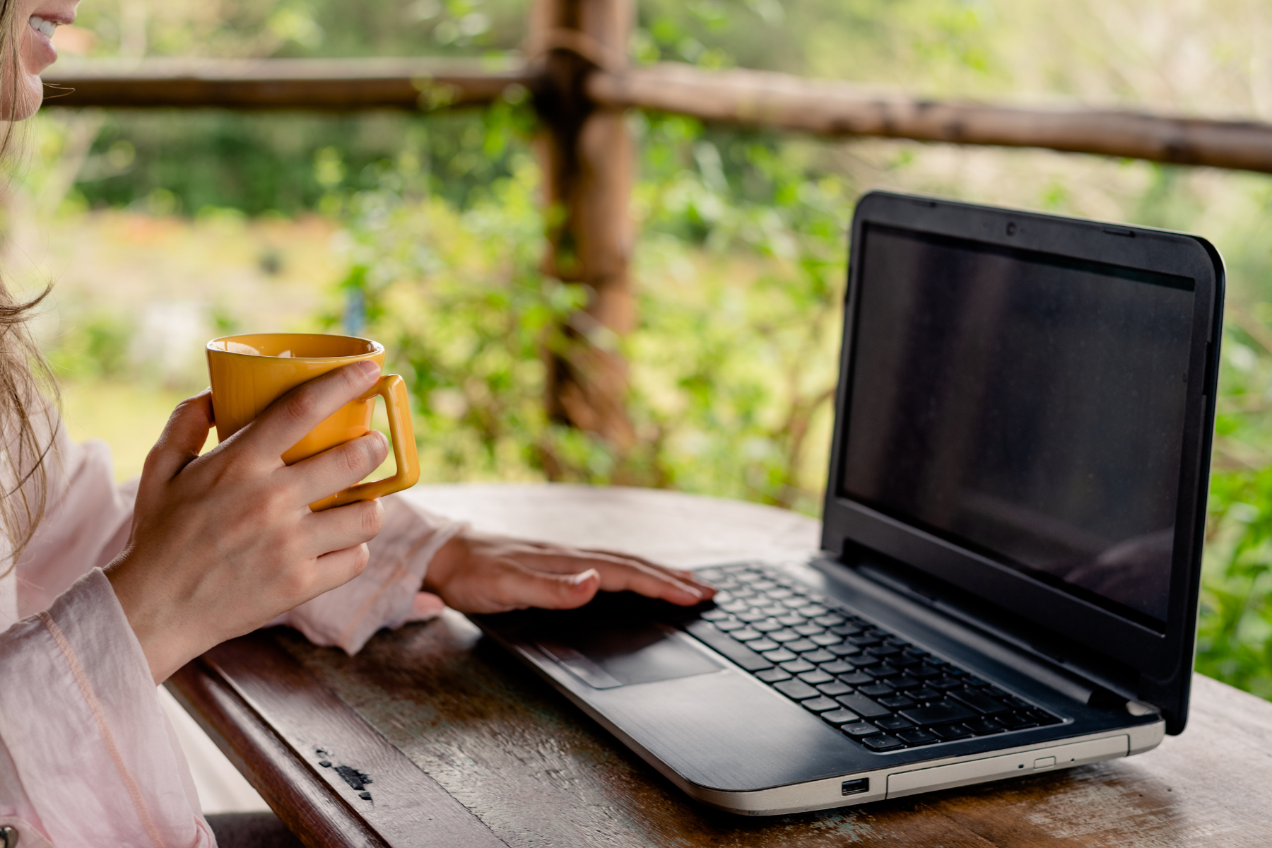 A woman at a laptop outdoors with a mug of coffee, on a video call.