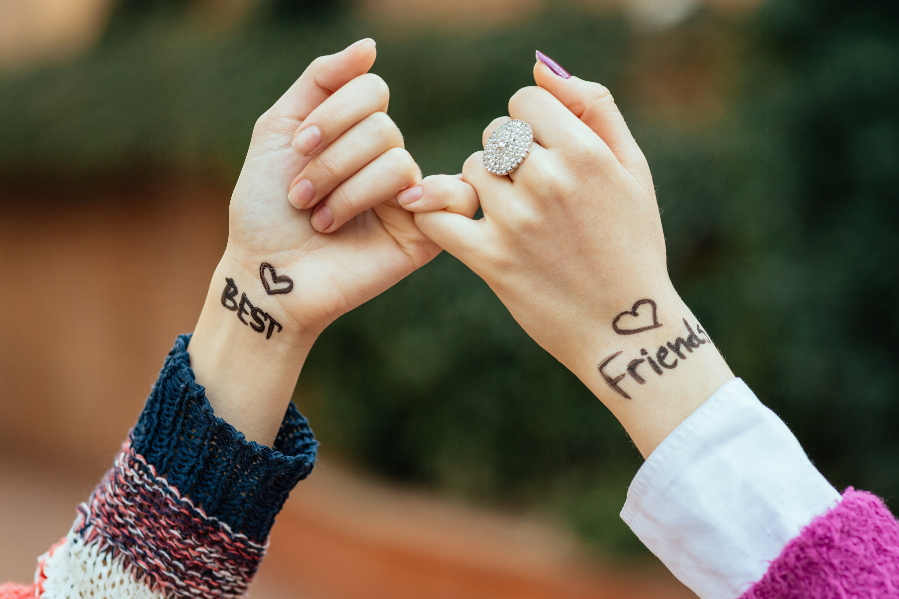 Two women linking pinky fingers, with "best friends" written on their wrists.