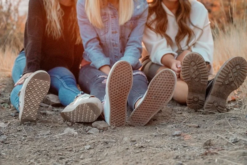 A group of women sitting together outdoors, feet touching in the center.