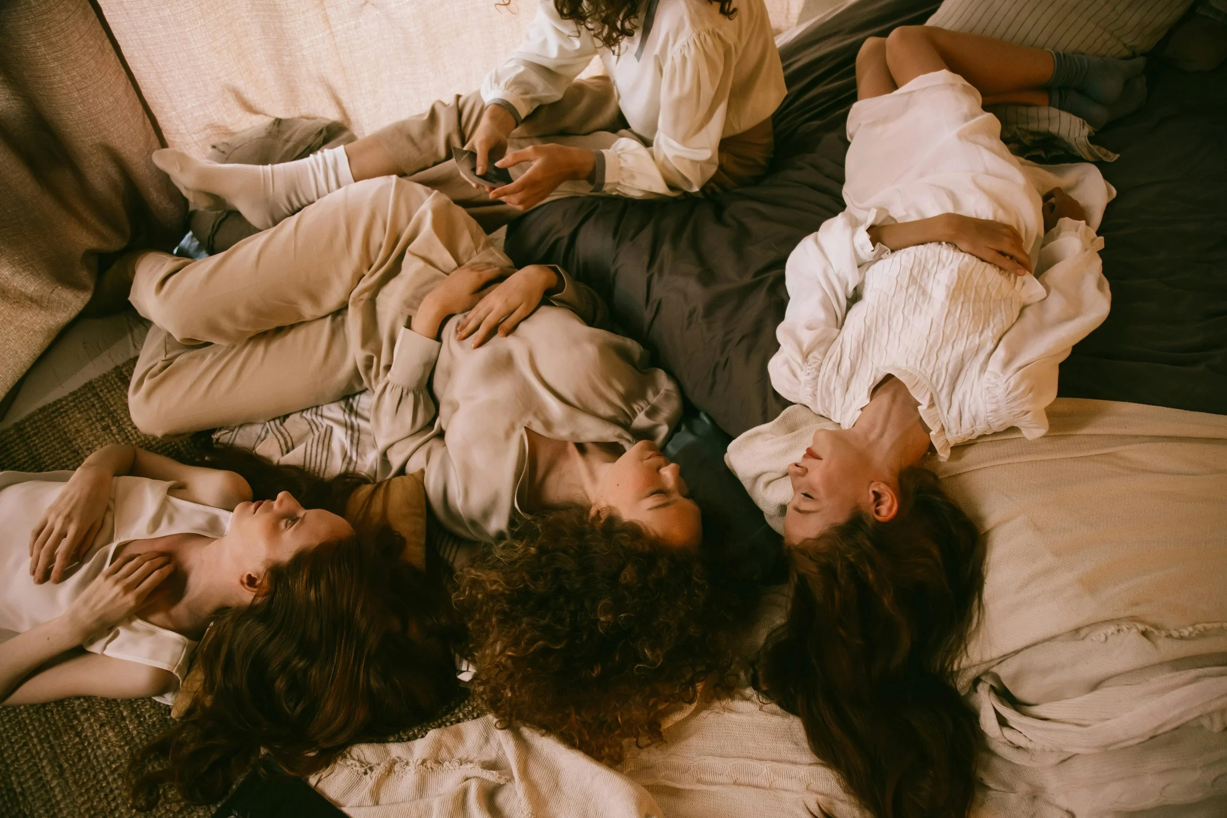 A group of women lying down together, heads to the center, talking and laughing.