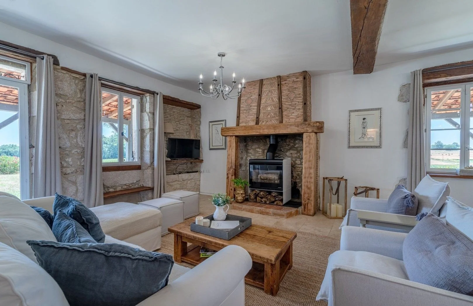 Living room with stone walls, wooden beams, a fireplace, and a flat-screen TV, with white sofas and a wooden coffee table.