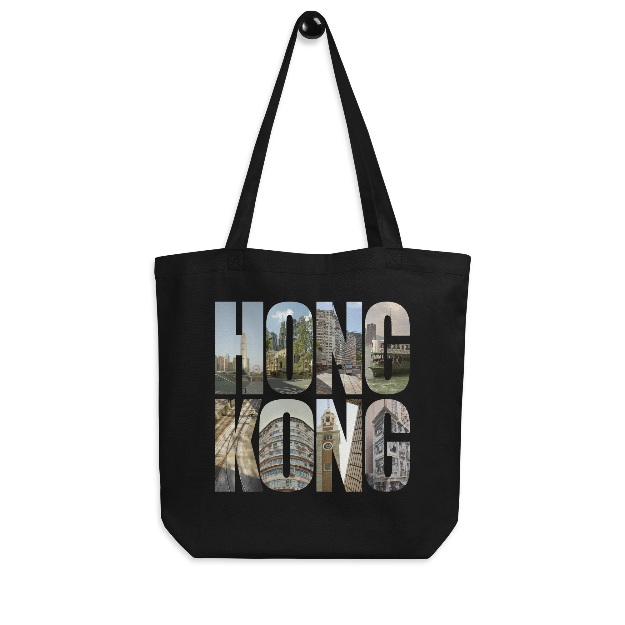 A black eco-friendly organic cotton tote bag. The front features the word "HONG KONG" printed in large block letters, with each letter containing authentic fine art photography of Hong Kong street sce
