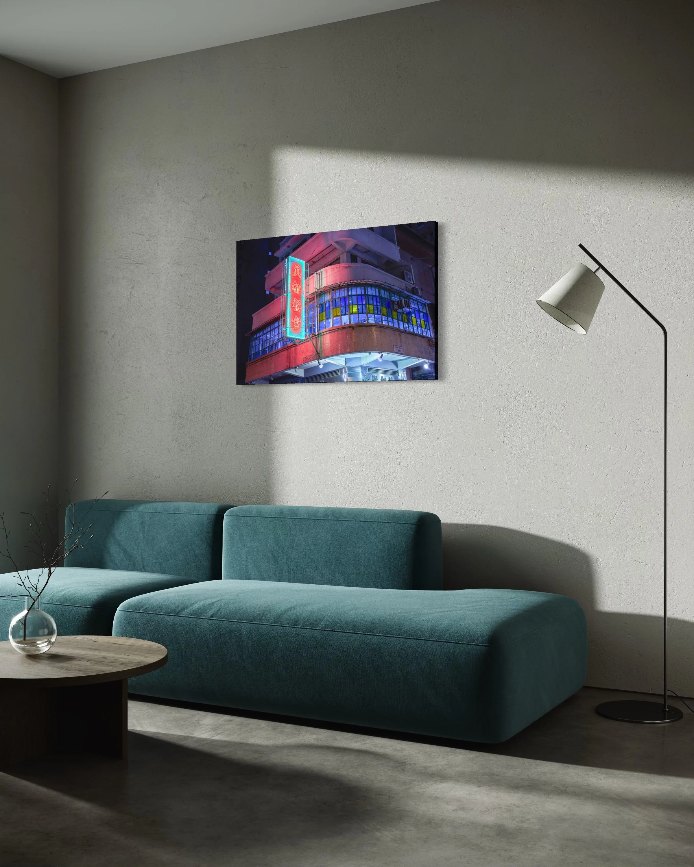 Interior of a living room featuring a teal sofa, a wooden coffee table with a glass vase. A wall-mounted picture of a building with neon lights hangs above the sofa. A modern floor lamp with a white shade and black arm is positioned beside the sofa. The room has neutral wall and carpet colors with natural light casting shadows.