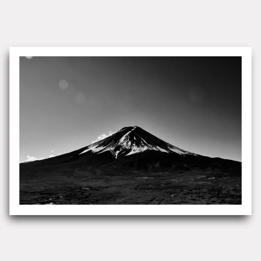 Black and white photograph of Mount Fuji in Japan, with a snow-capped summit and dark volcanic slopes under a pale sky.