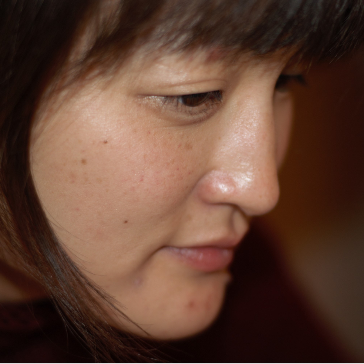 Close-up of a woman's face focusing on her cheek and eye, showing skin with freckles and small blemishes.