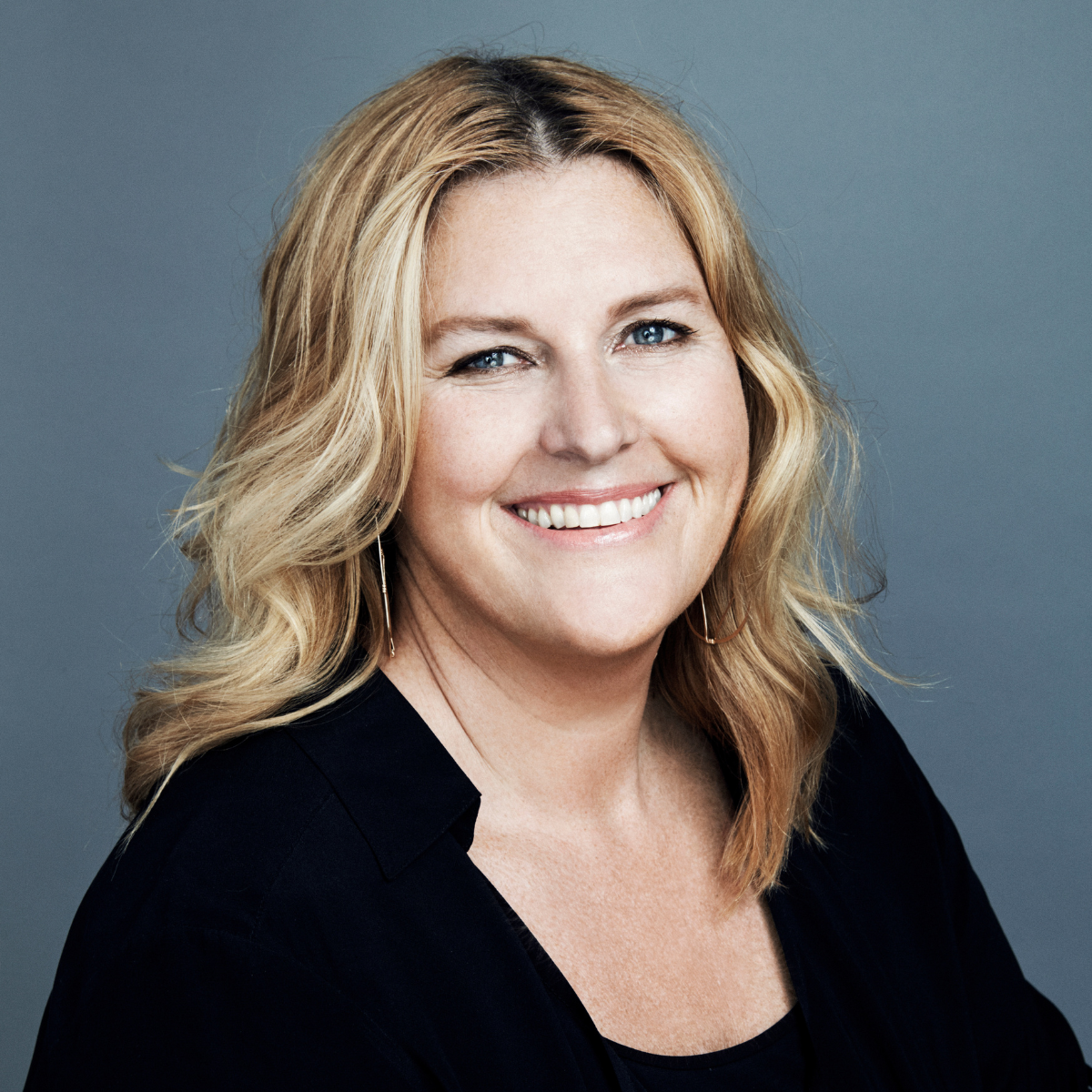 Headshot of a smiling woman with blonde hair wearing a black top against a gray background.