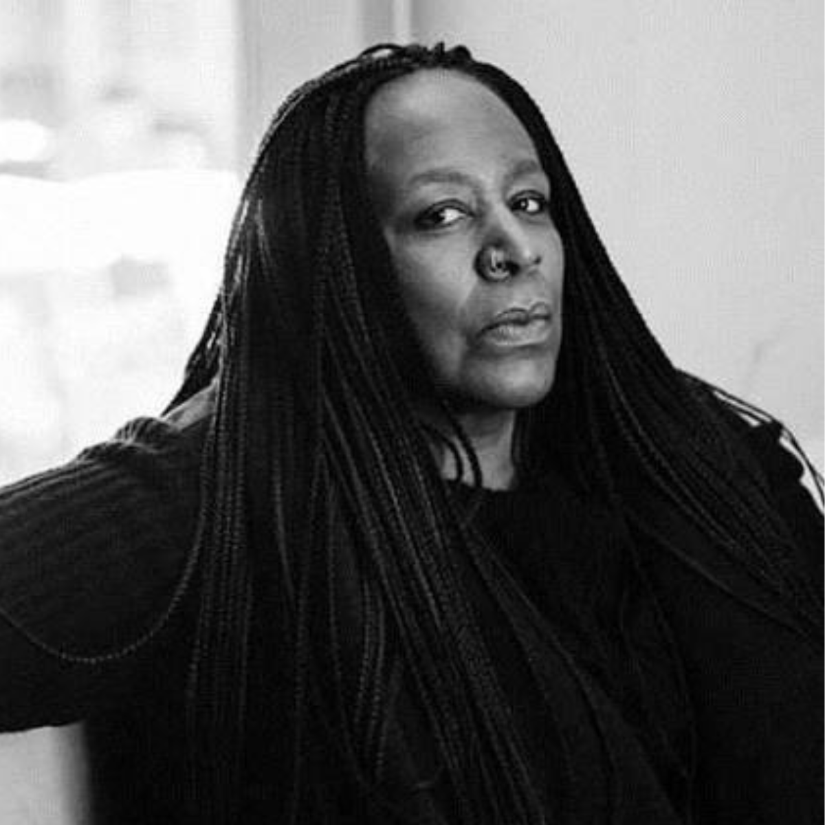 Black and white portrait of a woman with long braided hair, looking at the camera with a serious expression.