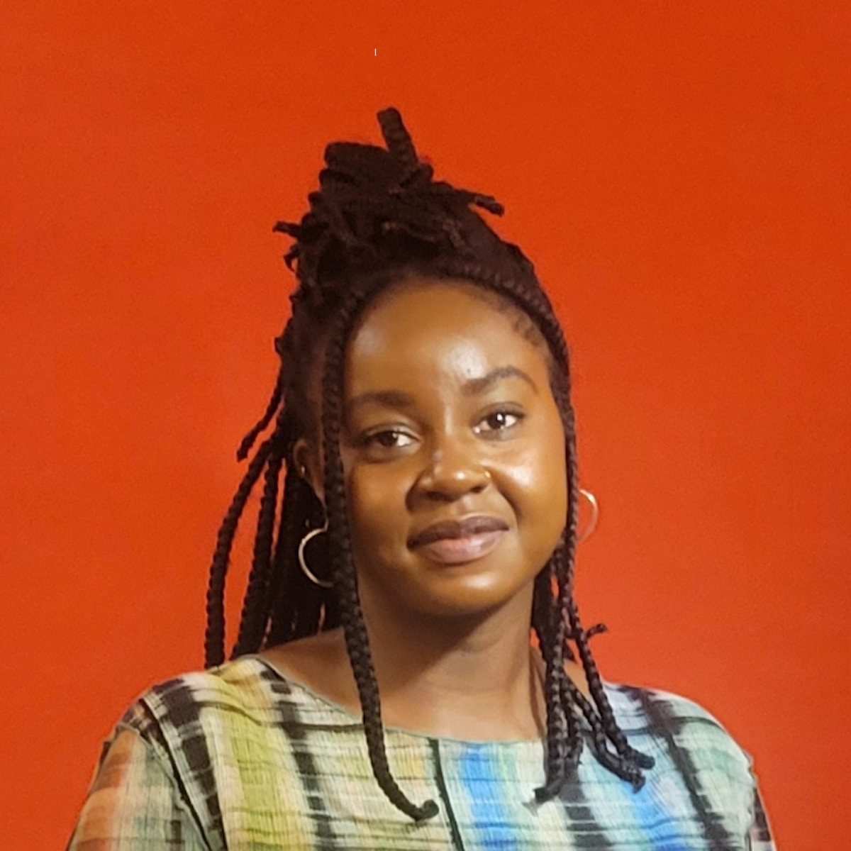 Portrait of a young woman with braided dreadlocks and hoop earrings, standing against an orange background.