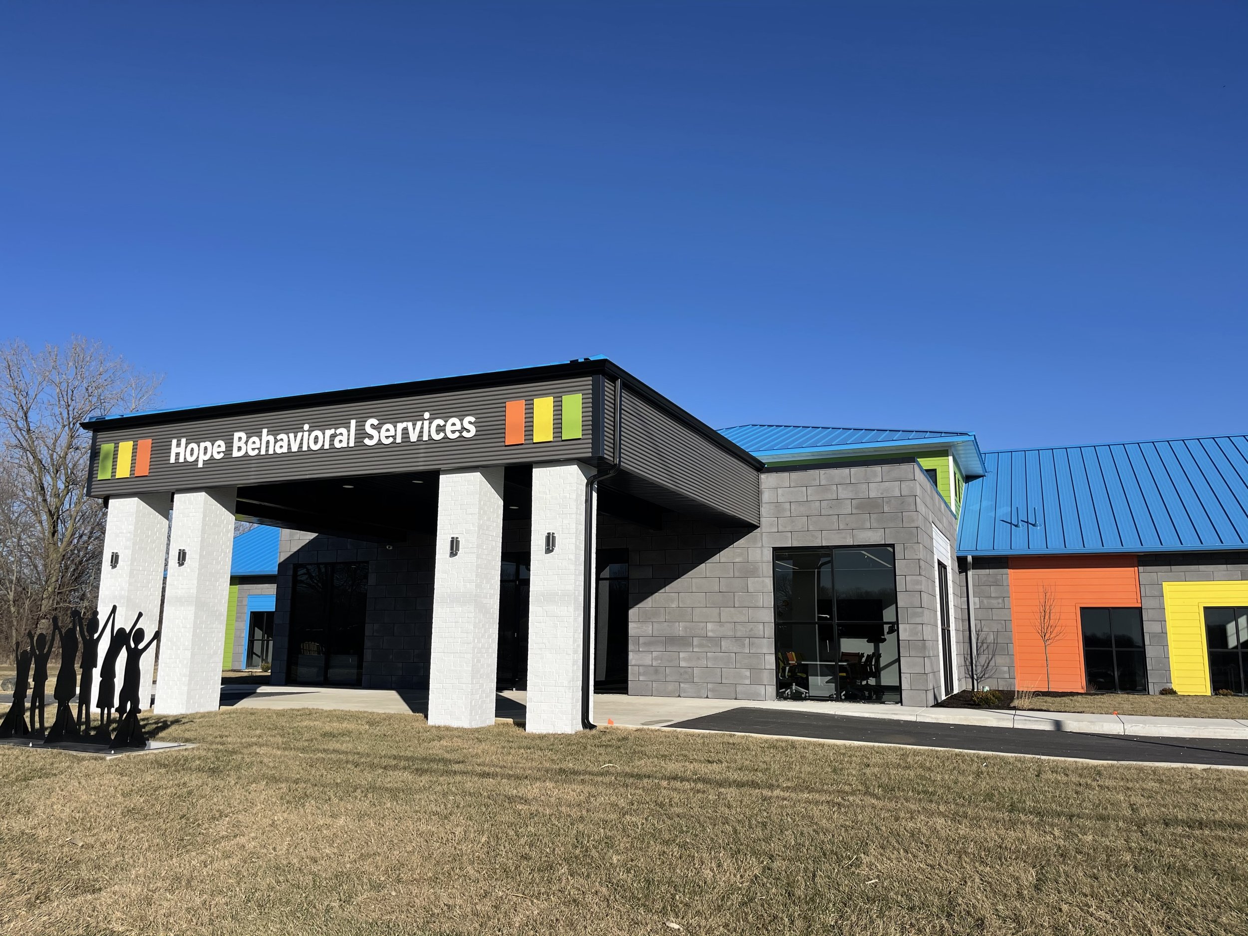 Exterior view of Hope Behavioral Services building with colorful accents, a manicured grass lawn, and a blue sky.