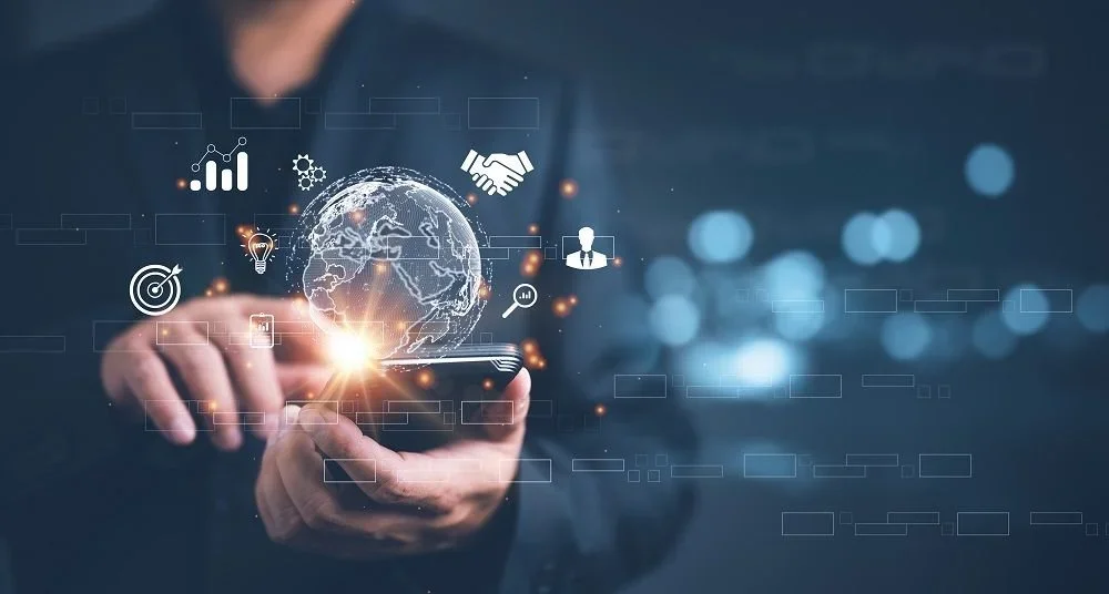 Person holding a smartphone with digital graphics of the globe, handshake, and business icons floating above.