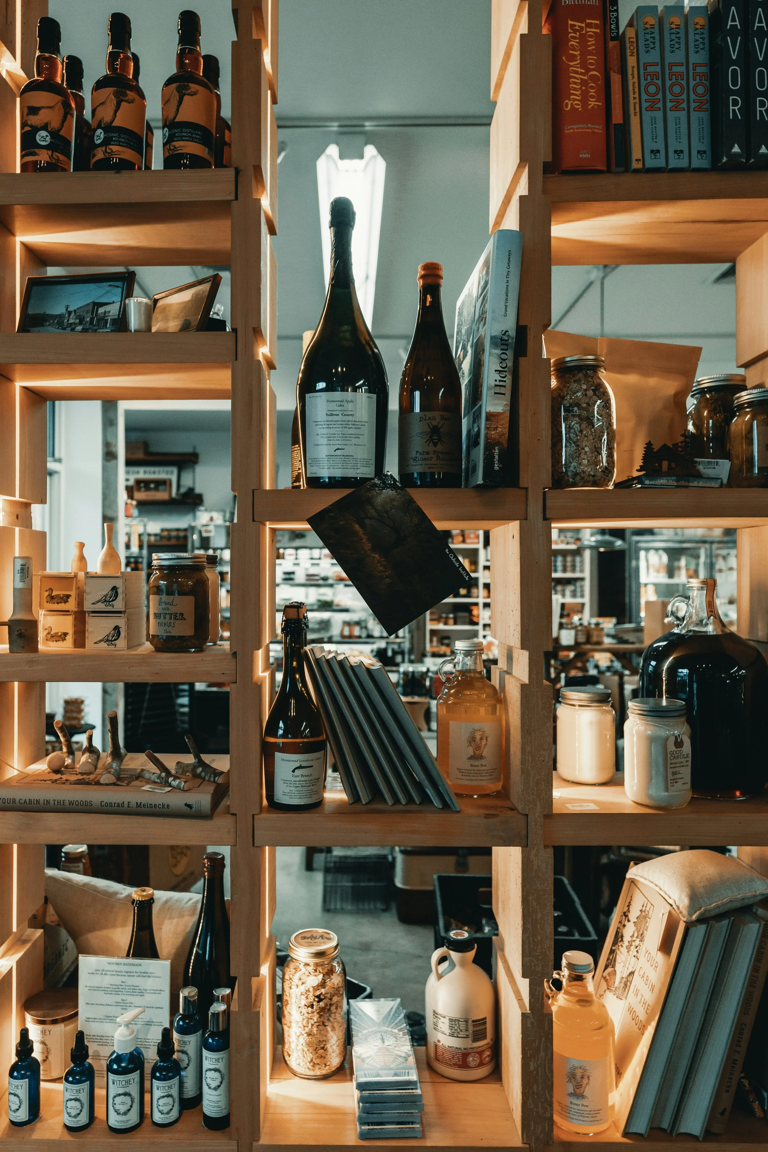 Wooden shelves filled with bottles, jars, books, and various decorative items inside a store or cafe.