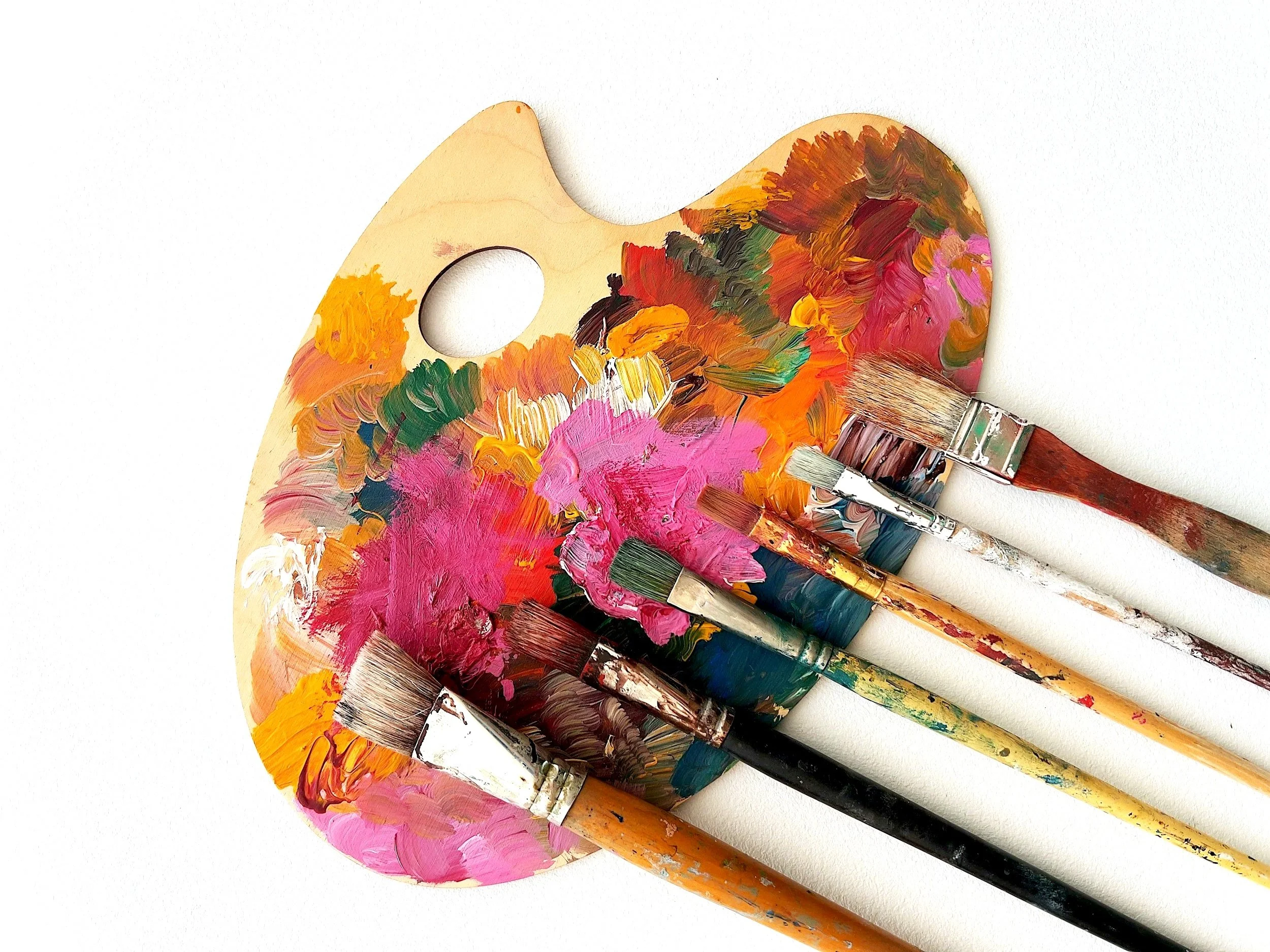 Paint palette with colorful blobs of paint and five paintbrushes dipped in paint, set against a white background.