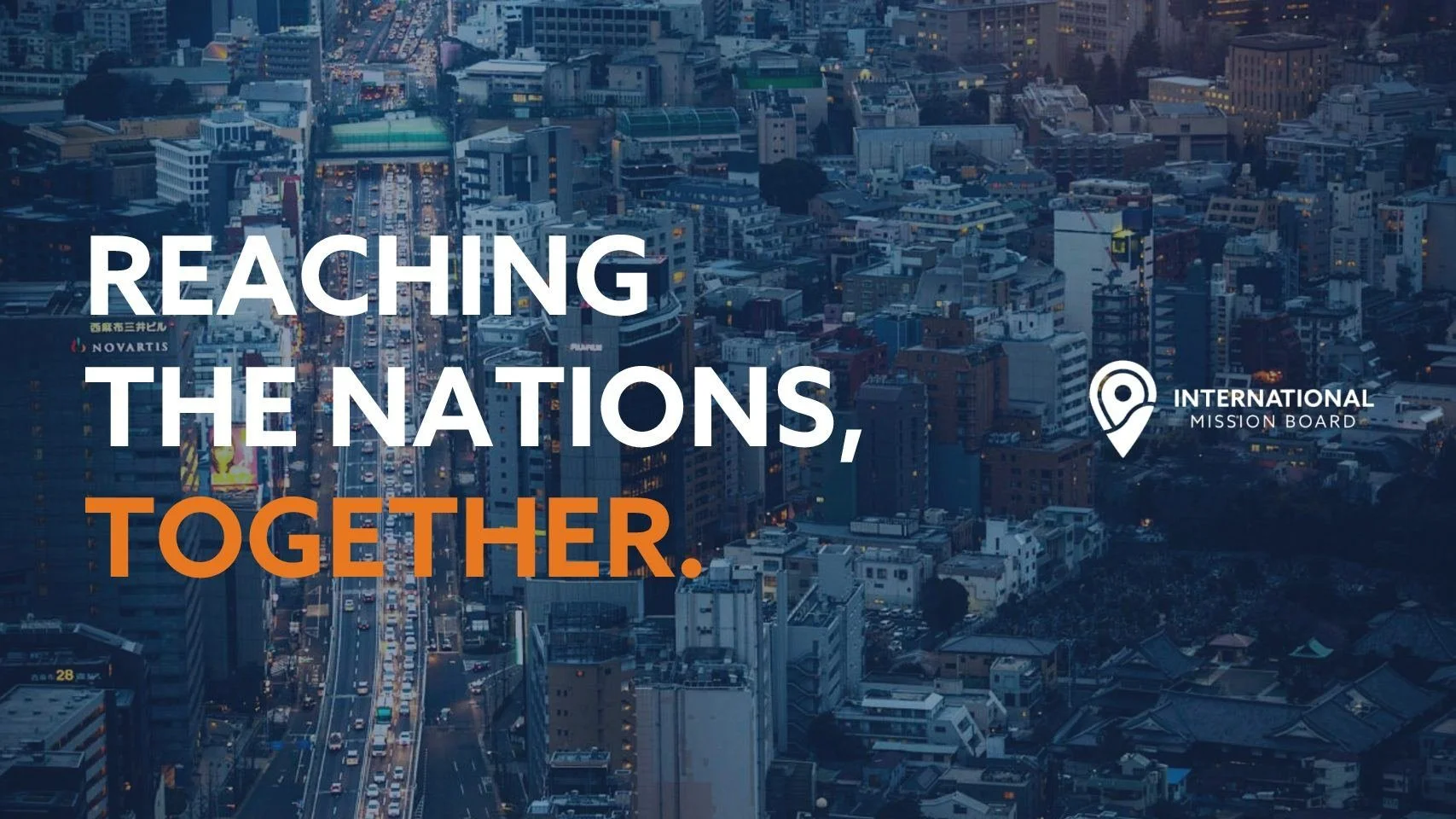 Aerial view of a city with a busy street, high-rise buildings, and city lights at dusk, overlaid with the text 'Reaching the Nations, Together' and a logo for the International Mission Board.