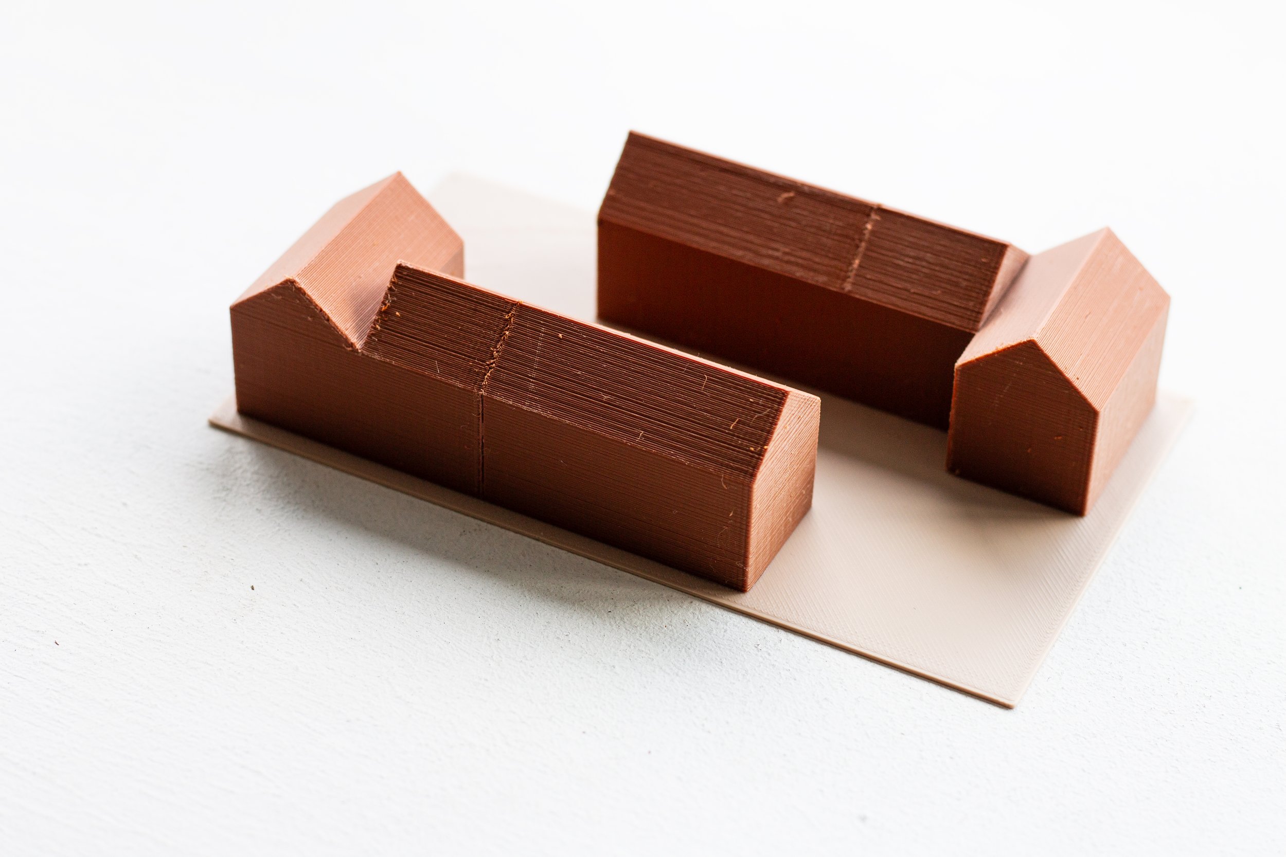 Two small rectangular blocks, one light brown and one dark brown, arranged to form a small structure on a white surface with a white background.