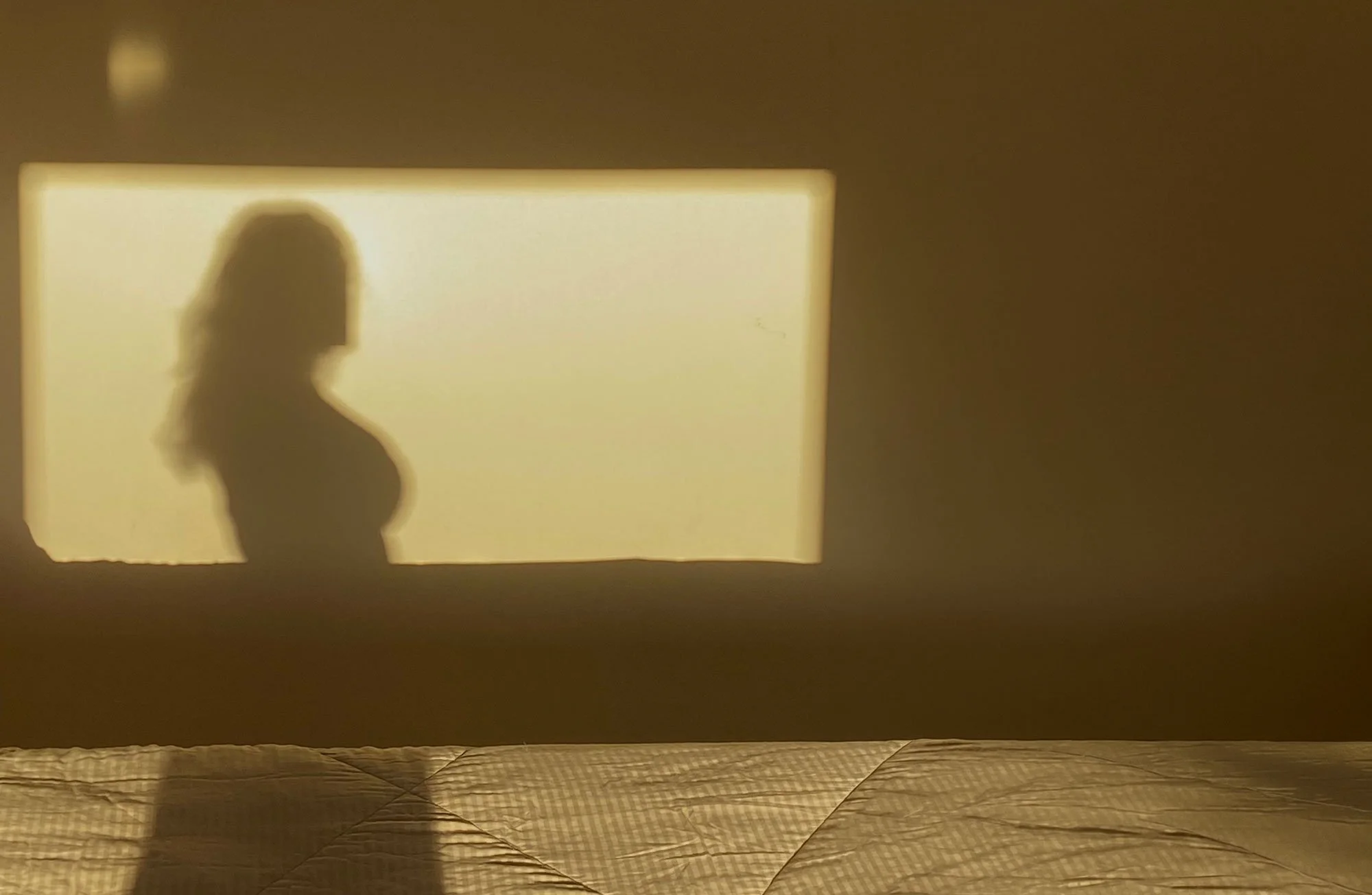 Silhouette d'une personne projetée sur un mur éclairé d'une lumière chaude dans une pièce sombre.