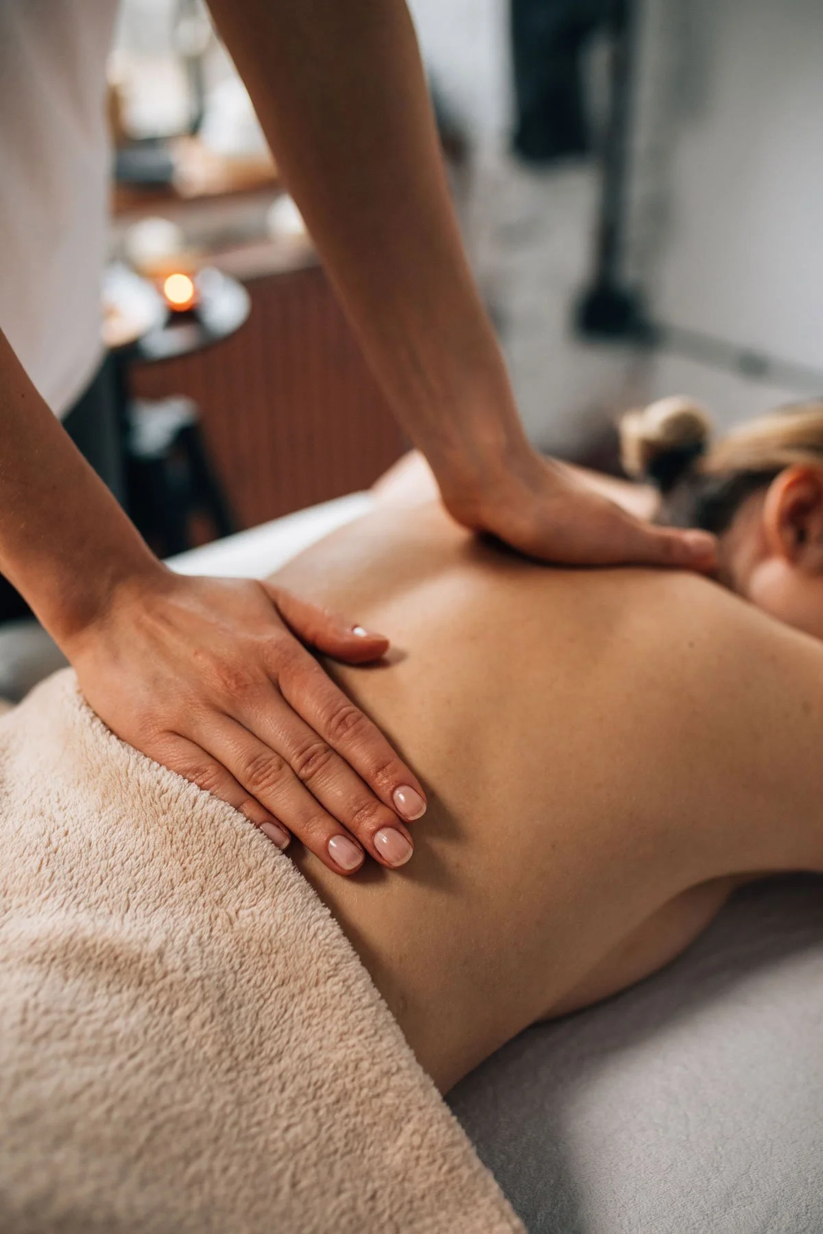 Une personne faisant un massage sur une autre personne allongée, avec une serviette beige recouvrant le corps de cette dernière.