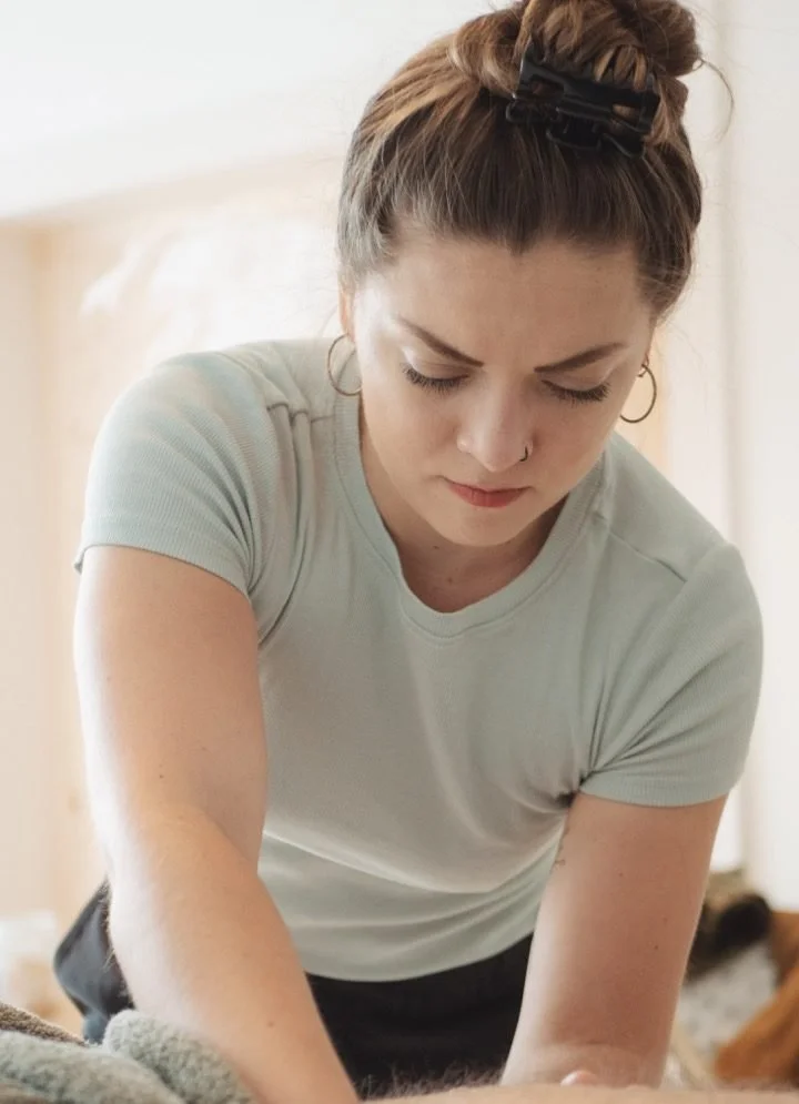 Une femme brune à cheveux attachés, portant un t-shirt gris effectue un massage.