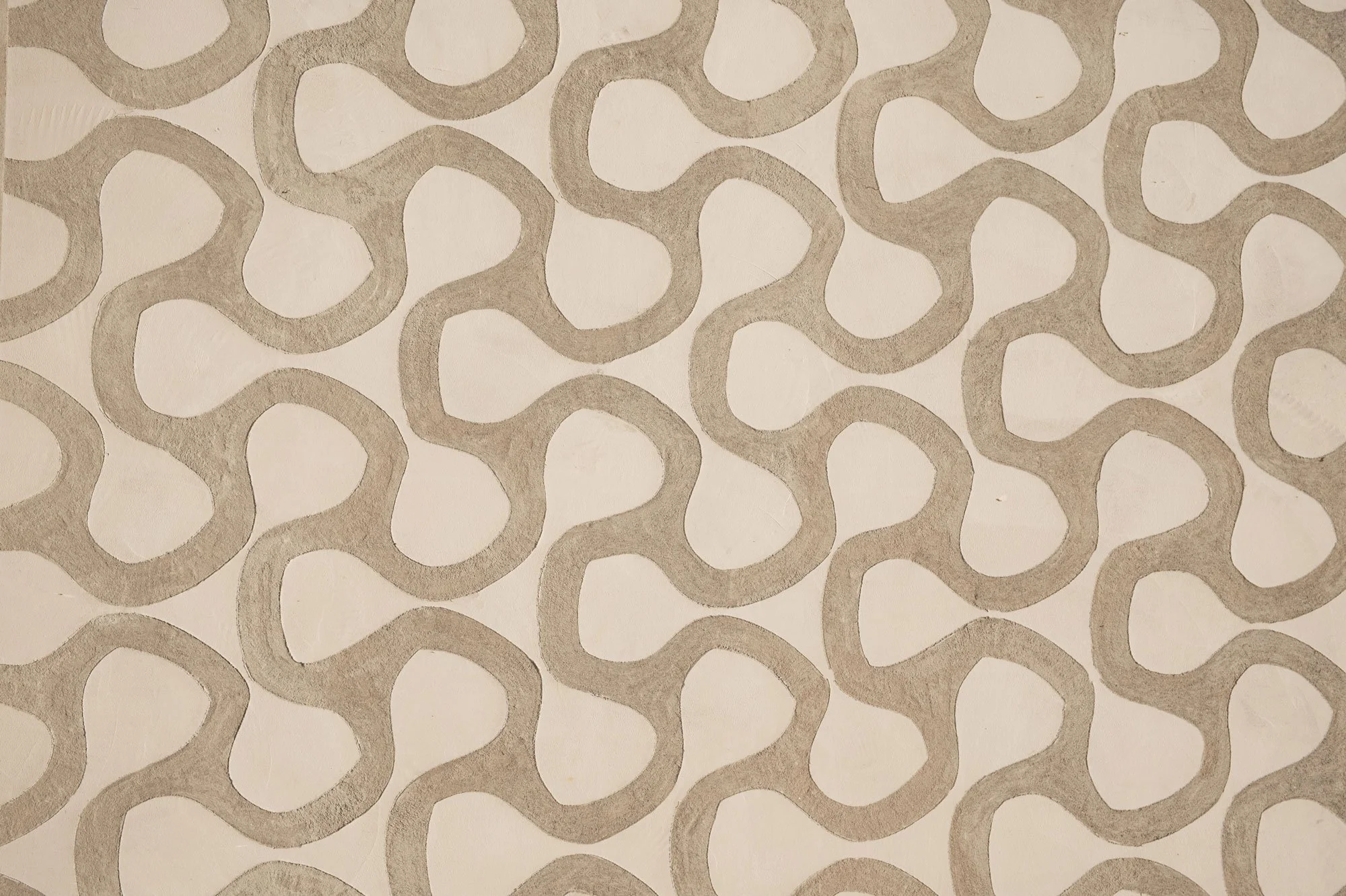 Motif géométrique composé de formes ressemblant à des anneaux ou des serpentins répétitifs en couleur beige ou taupe sur un fond clair.