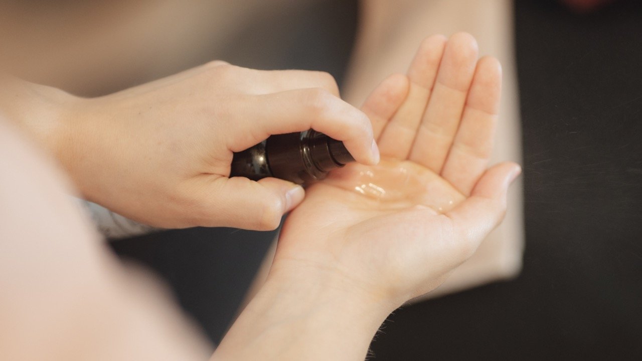 Une personne verse un liquide transparent dans la paume de sa main.