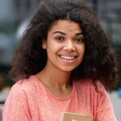 Jovencita sonriendo con cabello rizado,en un entorno urbano.