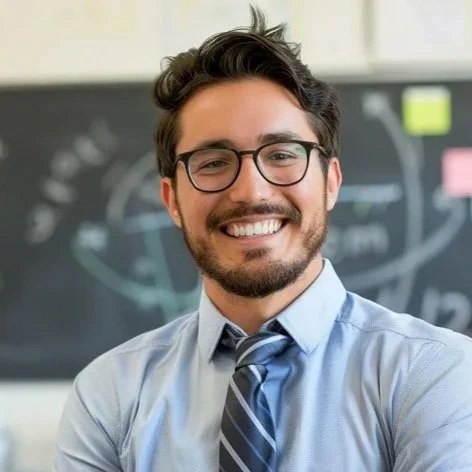 Profesor sonriendo en un aula con pizarra y notas adhesivas detrás.