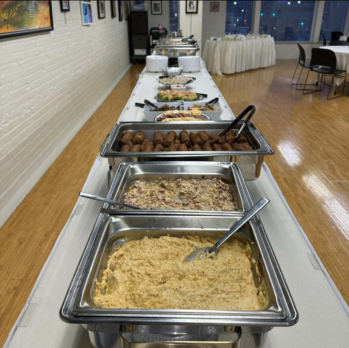 Buffet table with trays of mashed potatoes, meatloaf, meatballs, and other dishes at a catered event in a banquet hall.
