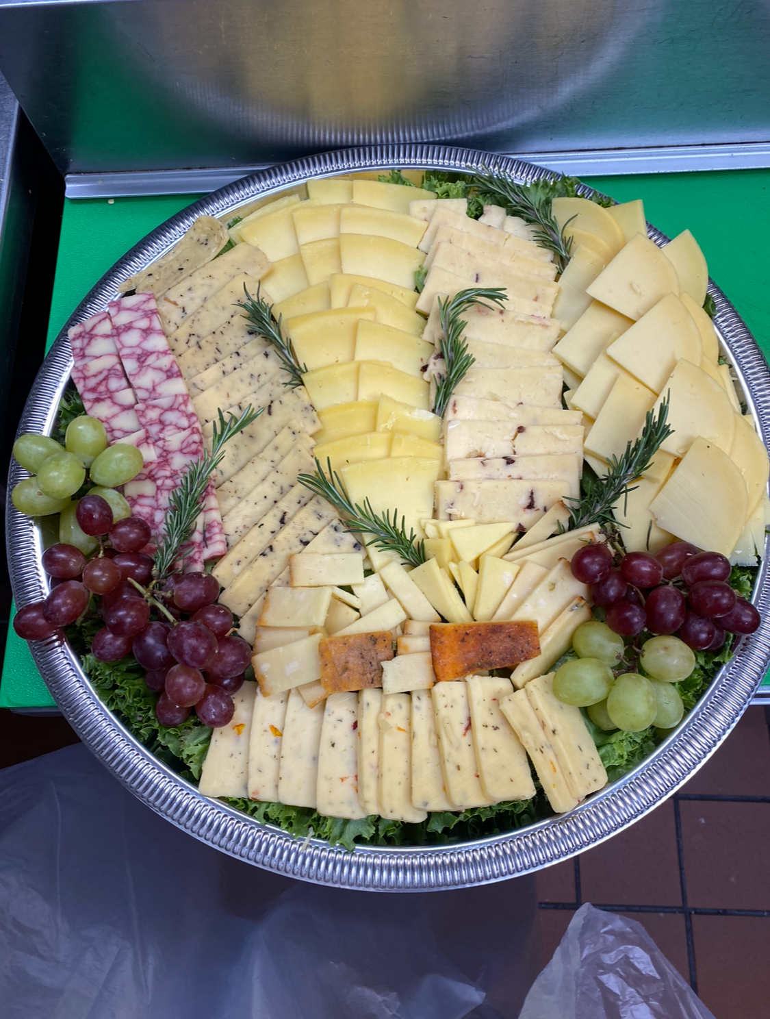 Assorted cheeses on a large silver platter, garnished with sprigs of rosemary and clusters of green and purple grapes.