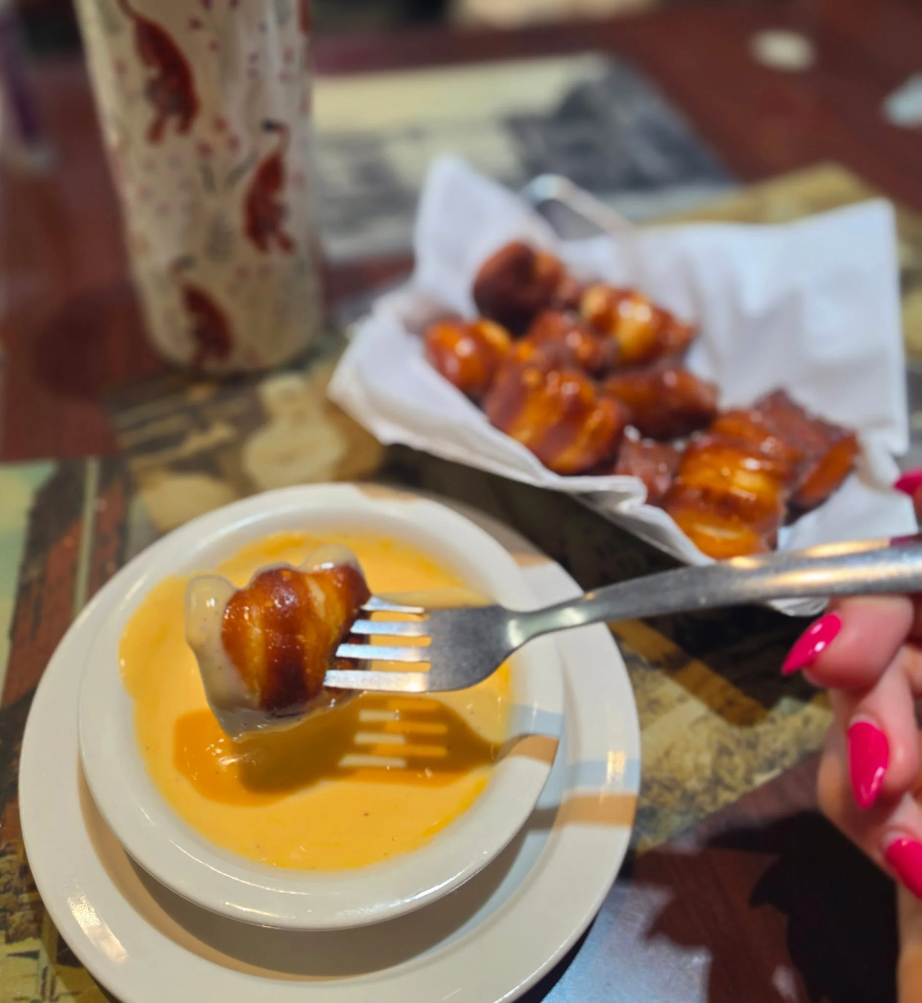 A fork with meatballs covered in sauce dipping into a bowl of yellow sauce on a white plate.