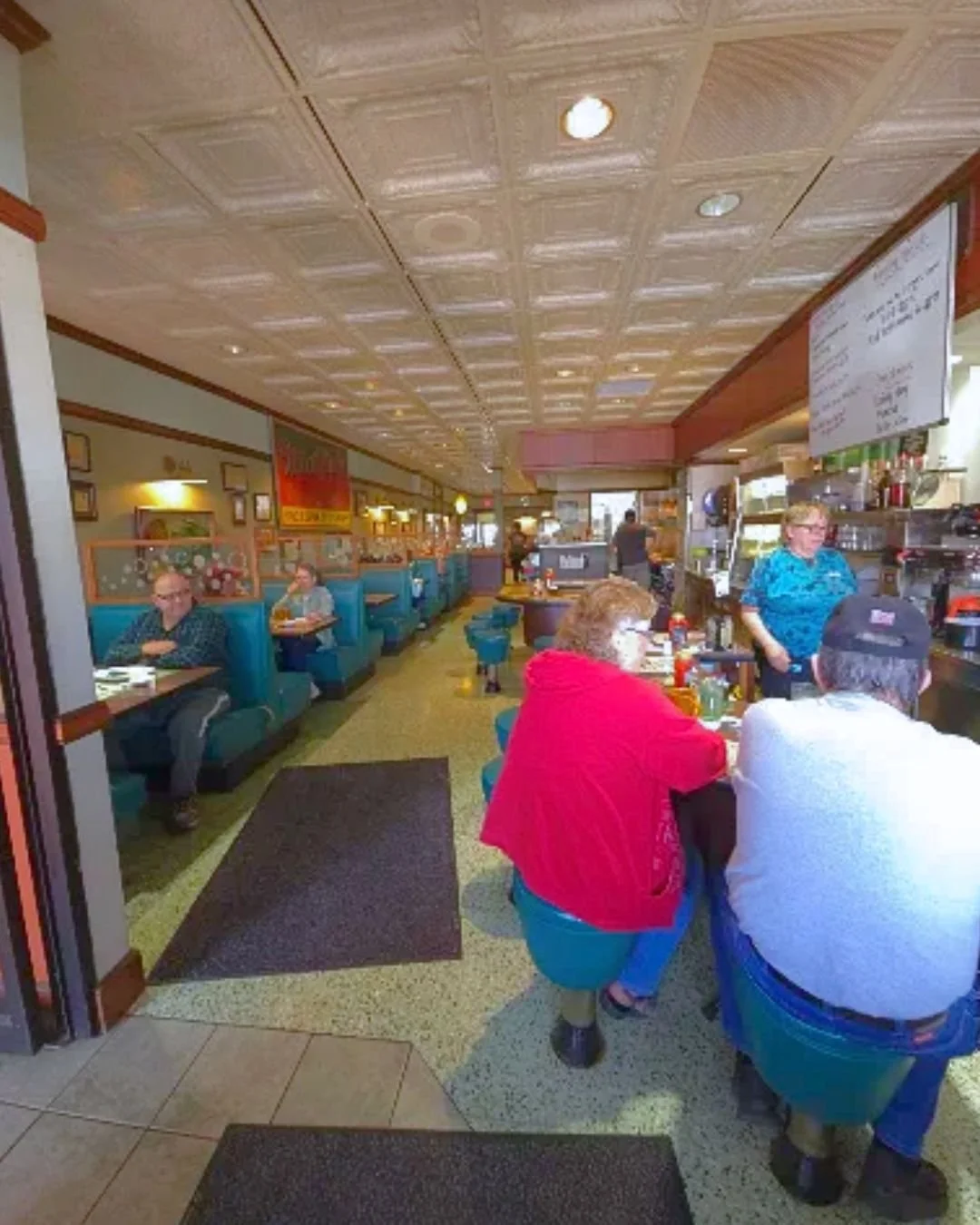 Inside a casual American diner with booths and a counter, patrons dining, and staff working behind the counter.